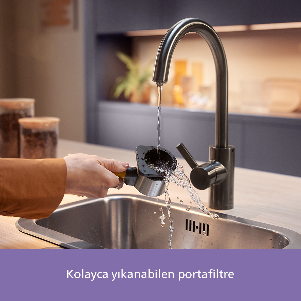 Bir el, bir kahve makinesi portafiltresini bir musluğun altında tutuyor. Musluktan akan su, portafiltreyi bir lavabonun üzerinde temizliyor.