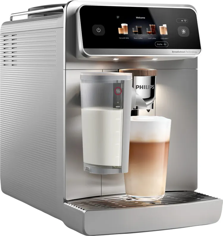 Egy ezüst Philips eszpresszógép egy pohár latte-val. A bal oldalon egy tejeskanna található. A gép digitális képernyővel rendelkezik.