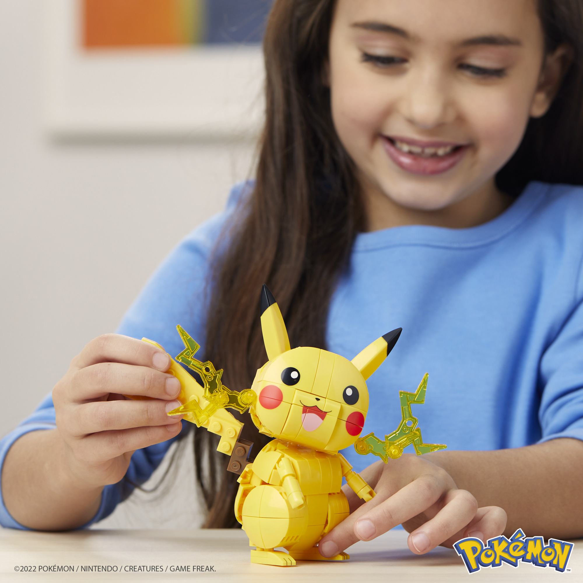 Ein lächelndes Mädchen hält eine gelbe Pikachu-Lego-Figur. Es hat Blitze. Der Hintergrund ist verschwommen.
