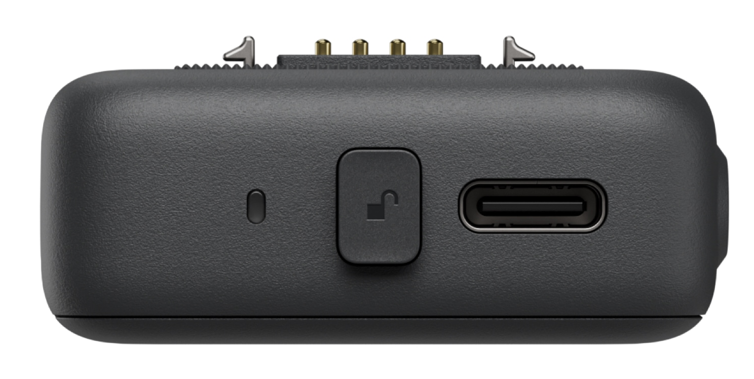 Egy sötétszürke eszköz USB-C porttal, egy feloldás szimbólummal ellátott gombbal és fém csapokkal. Texturált felülete van.