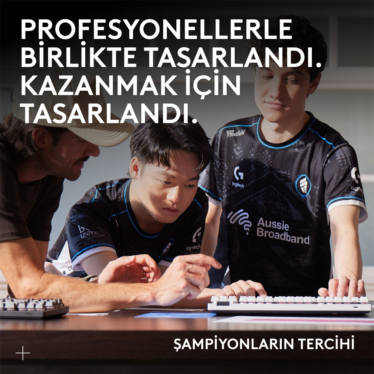 Üç adam klavyeye bakıyor, üstte metin var. Bir adam şapka takıyor, diğerleri logolu siyah gömlekler giyiyor, önünde bir klavye var.