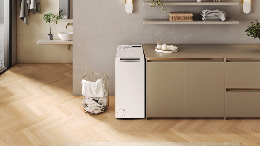 Un lave-linge blanc se trouve dans une buanderie moderne. Un panier doré avec des serviettes est à gauche. Plancher en bois.