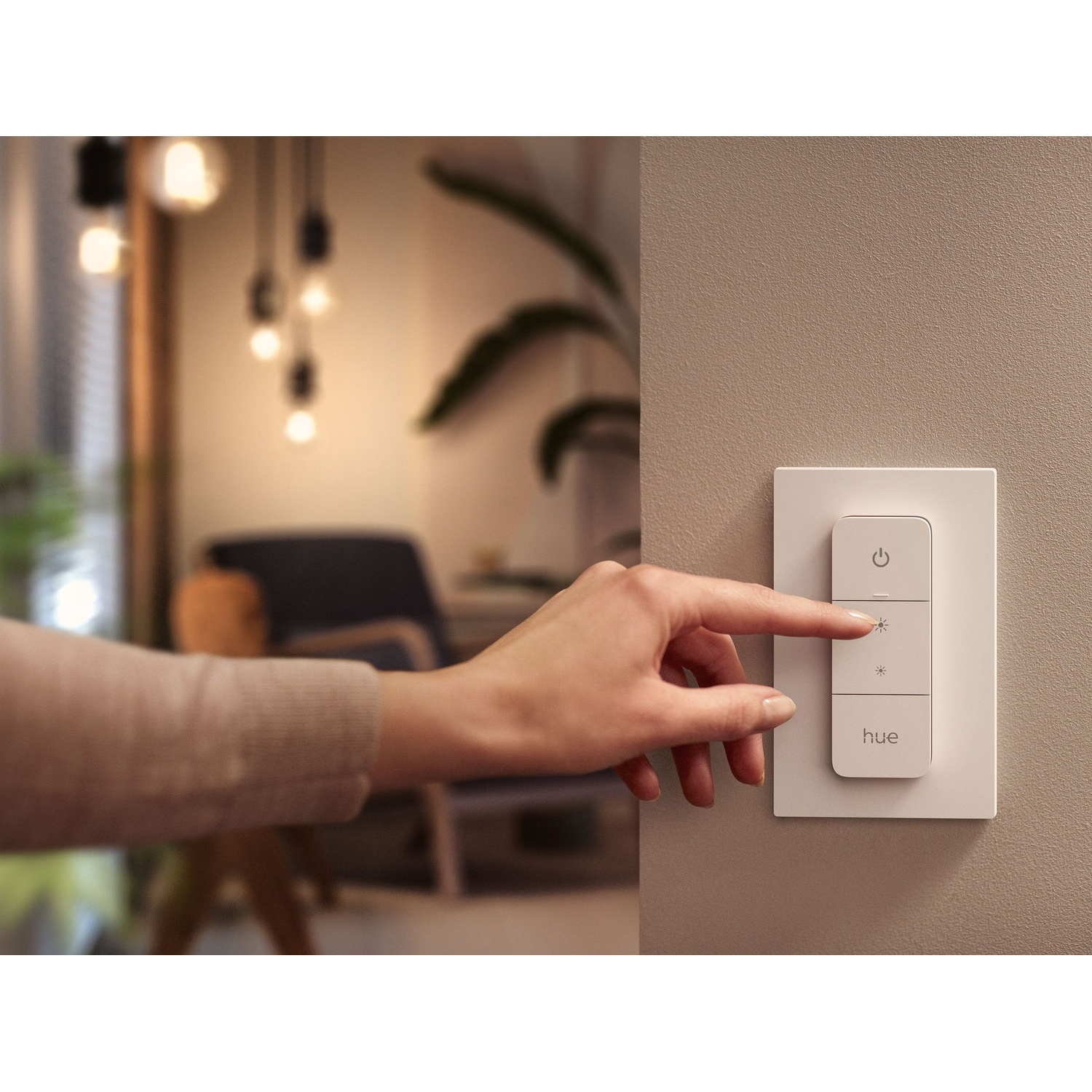 Una mano preme un interruttore sulla parete. L'interruttore ha tre pulsanti: accensione/spegnimento, luminosità e attenuazione. Il marchio è 'hue'.