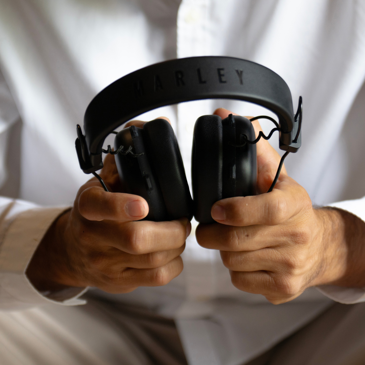 A person is holding black Marley headphones. The person wears a white shirt. The headphones have the word 'MARLEY' on the top.