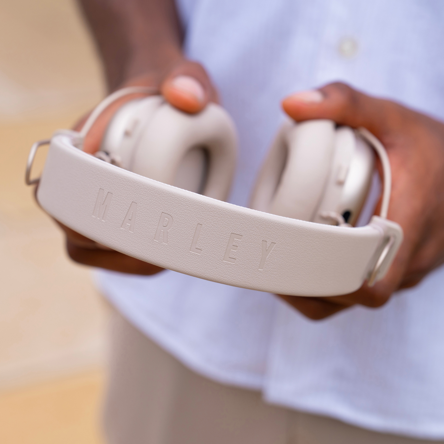 Une personne tient un casque Marley beige. Le bandeau affiche le nom de la marque. Une chemise blanche est visible en arrière-plan.