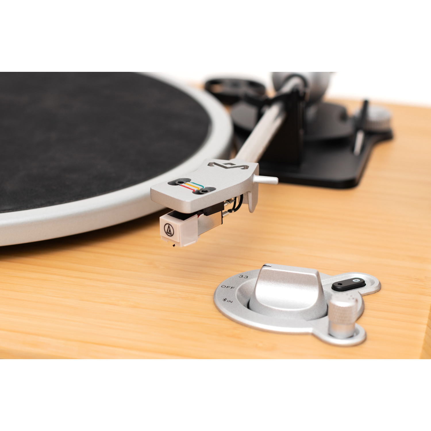 Close-up of a record player with a silver tone arm, black platter, and wooden base. A control knob is visible.