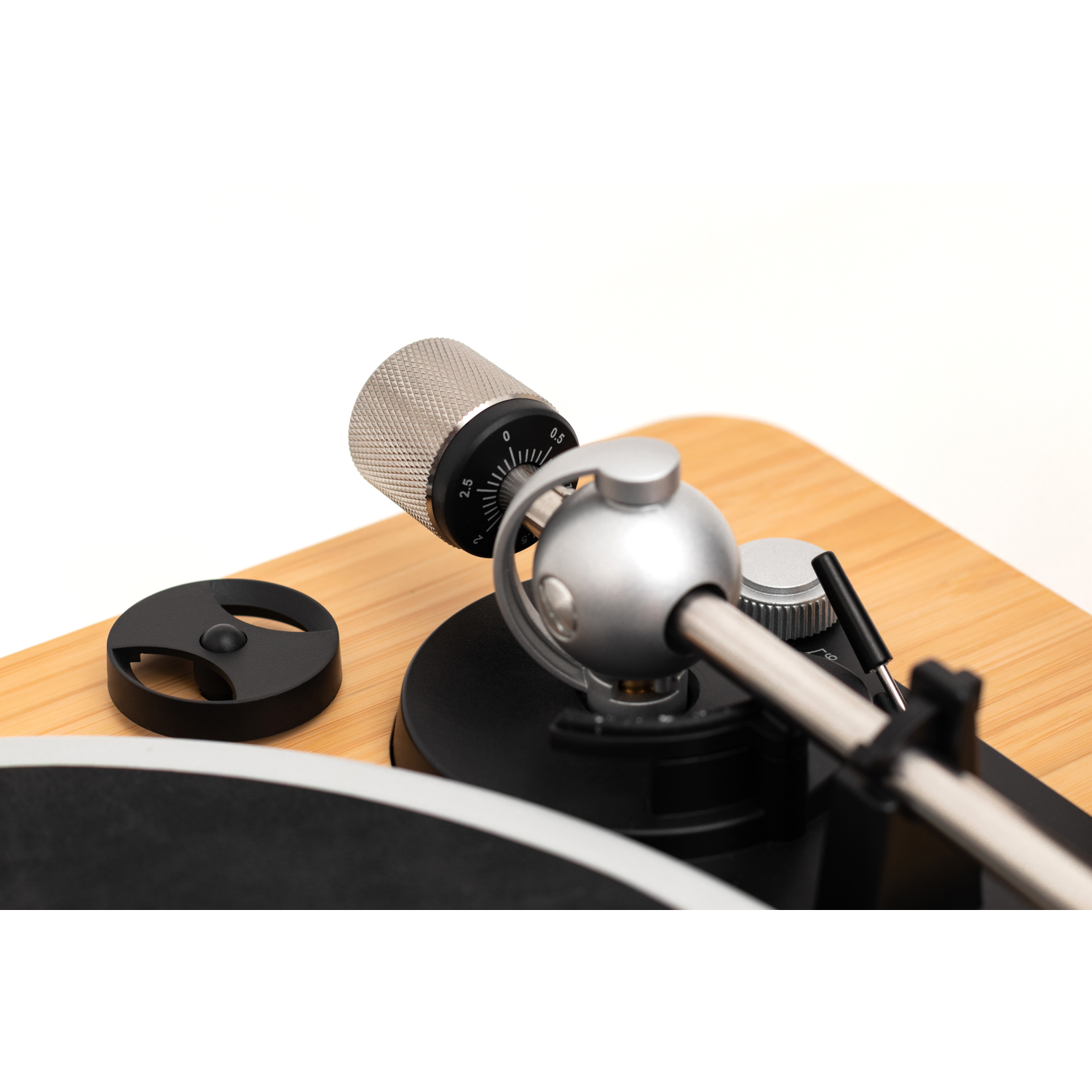 Close-up of a turntable. Silver arm, dial, and knob. Black disc and base on wooden surface. White background.