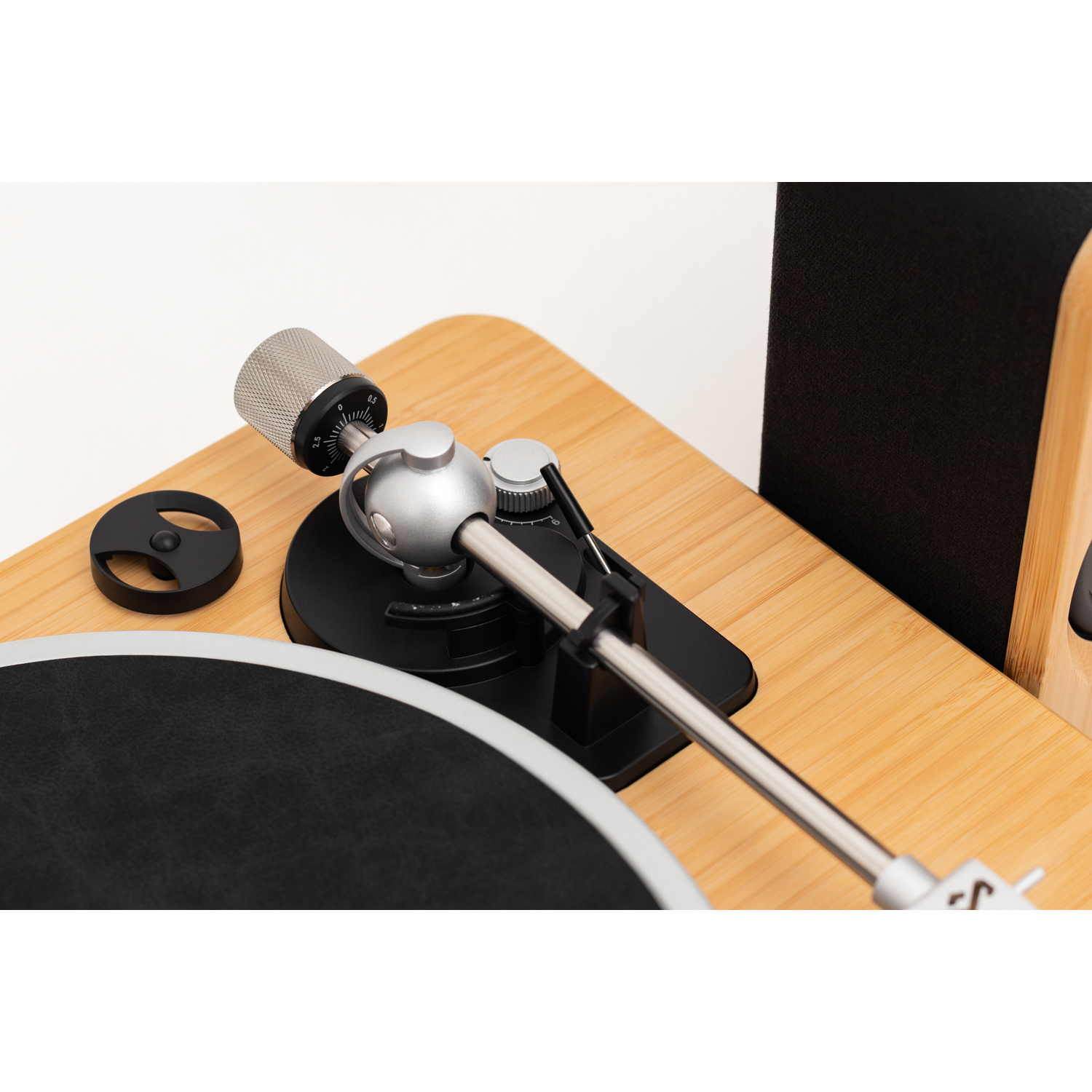 A turntable with a silver tonearm and black record. It's on a bamboo-style surface, and a black speaker is visible.