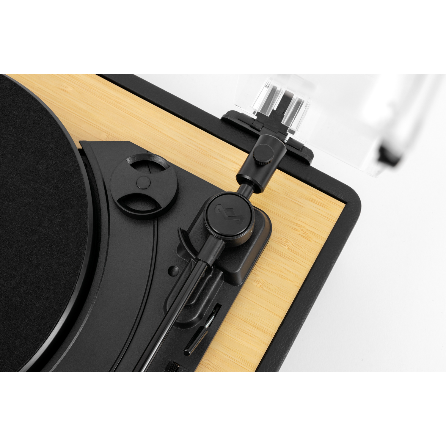 Close-up of a record player. The turntable is black with a bamboo wood base. The tone arm and cover are clear plastic.