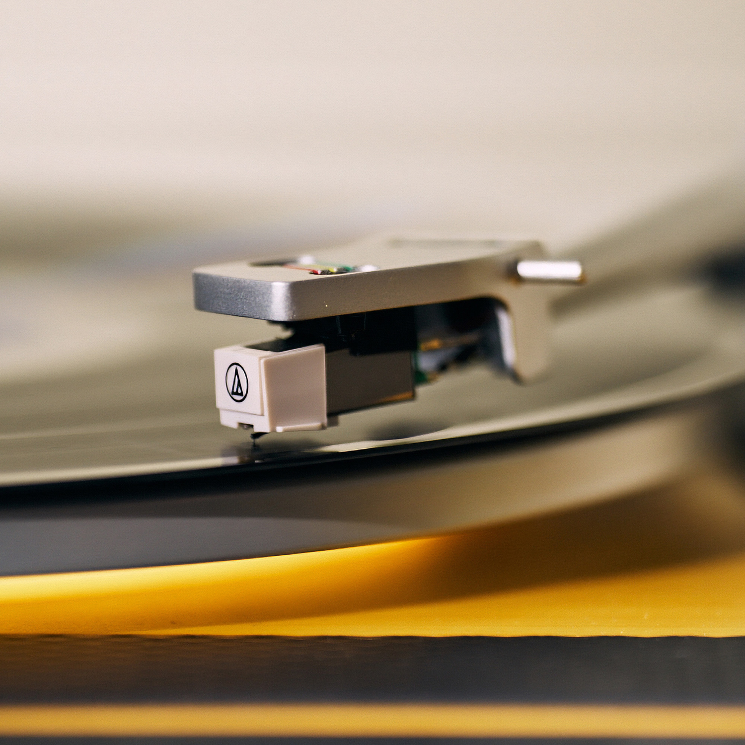 Close-up of a record player needle on a spinning record. The needle is silver and white, with a black record.
