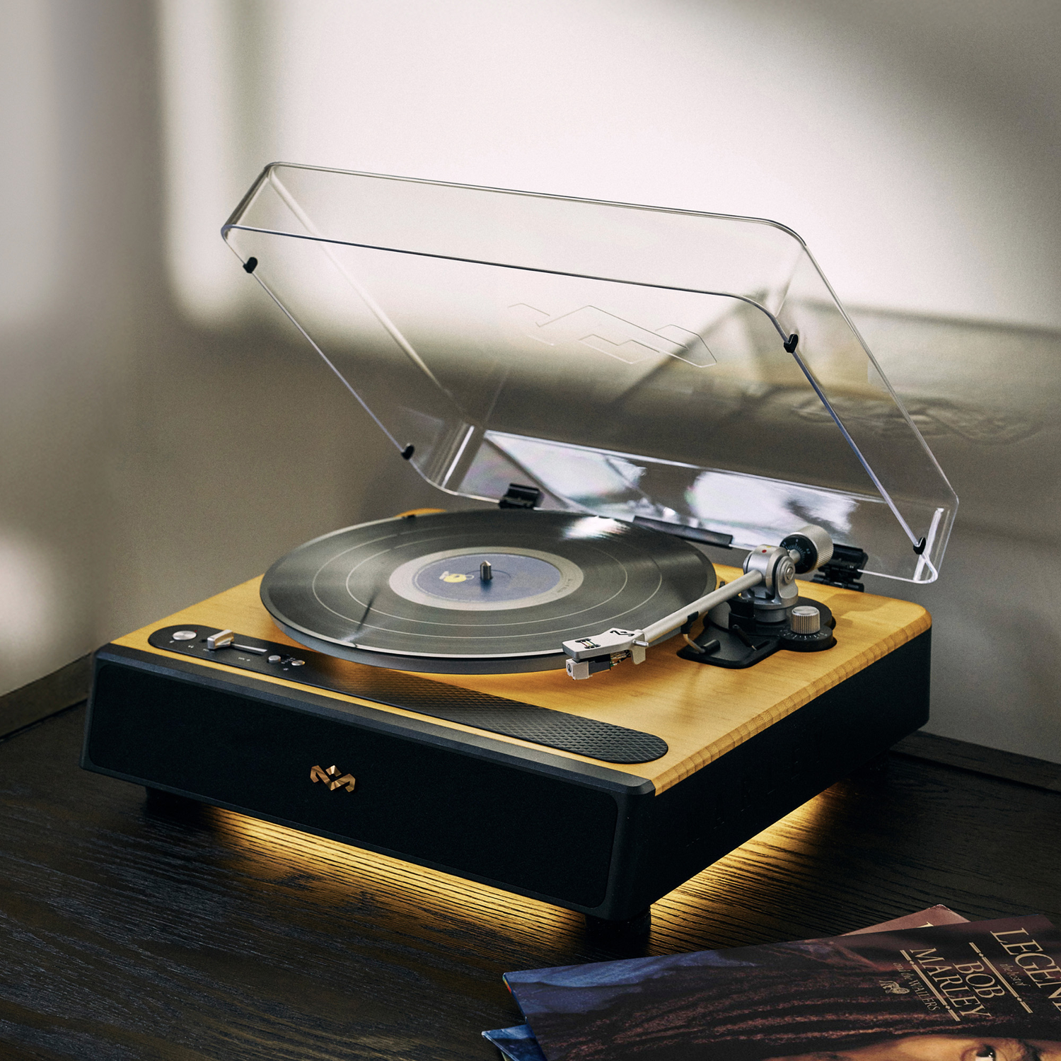 A turntable with a record playing. It sits on a dark wooden surface. The cover is up. There is a Bob Marley album nearby.