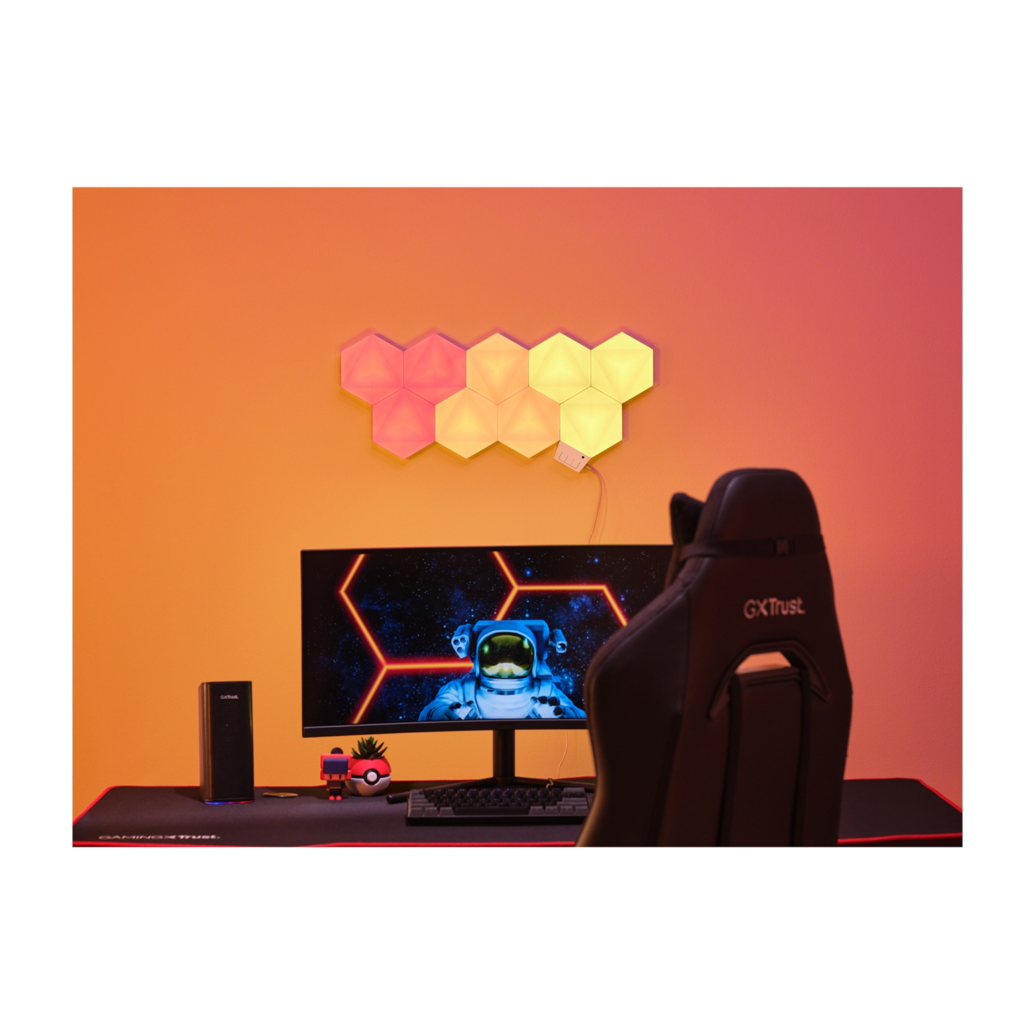 Configurazione di gioco con monitor astronauta, luci esagonali, sedia e accessori su una scrivania.
