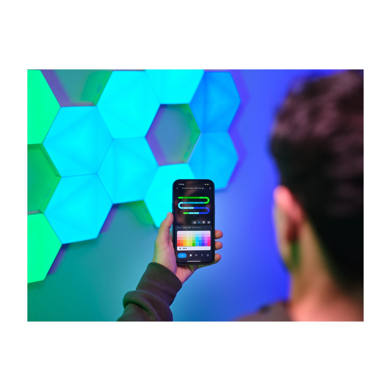 Una persona tiene in mano un telefono che controlla luci esagonali su un muro. Le luci sono di varie tonalità di blu e verde.