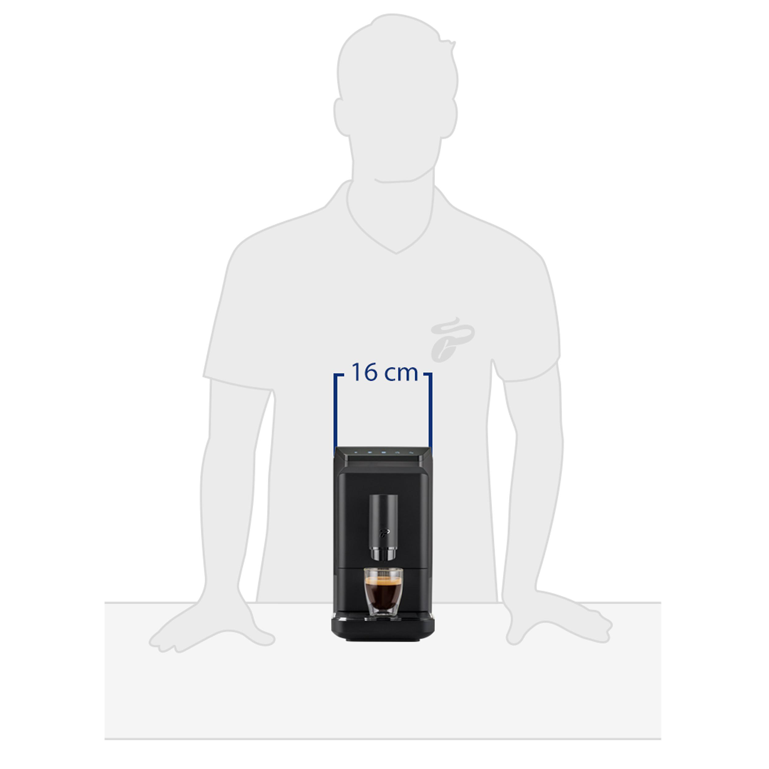 Eine Person steht hinter einem Tisch. Auf dem Tisch steht eine schwarze Kaffeemaschine mit einem Espresso.