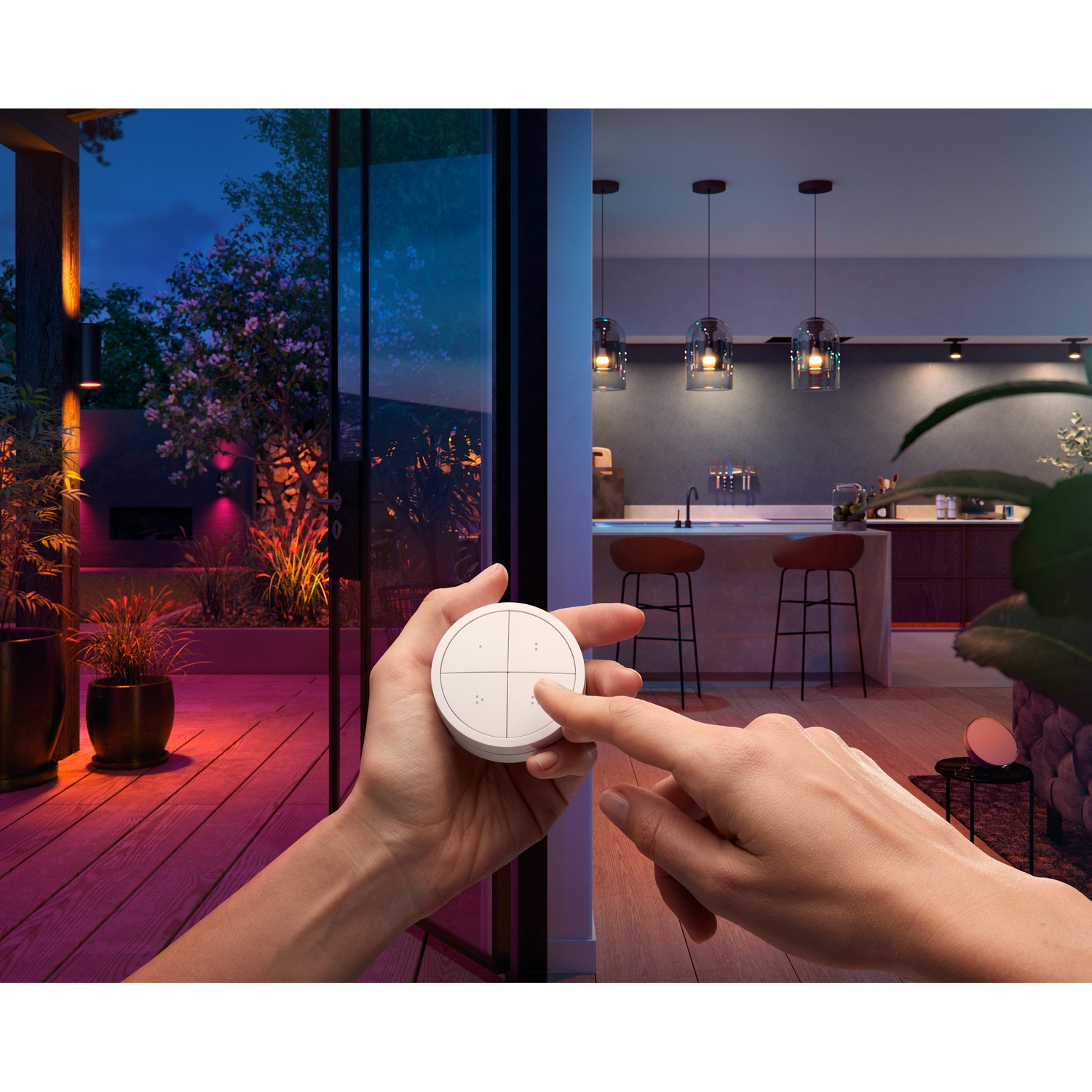 Una mano tiene in mano un dispositivo per la casa intelligente. All'esterno, un patio con piante e luci. Sullo sfondo, una cucina.