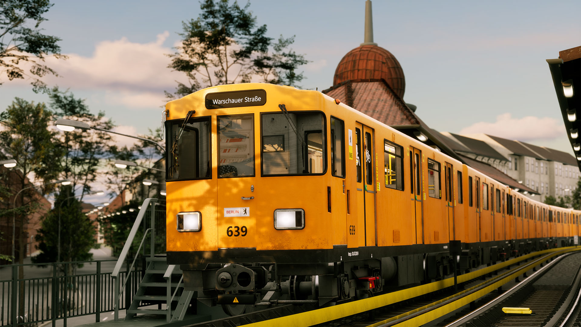 Ein orangefarbener Berliner U-Bahn-Zug am Bahnhof Warschauer Straße. Der Zug befindet sich in einem Tunnel mit Gebäuden und Bäumen im Hintergrund.