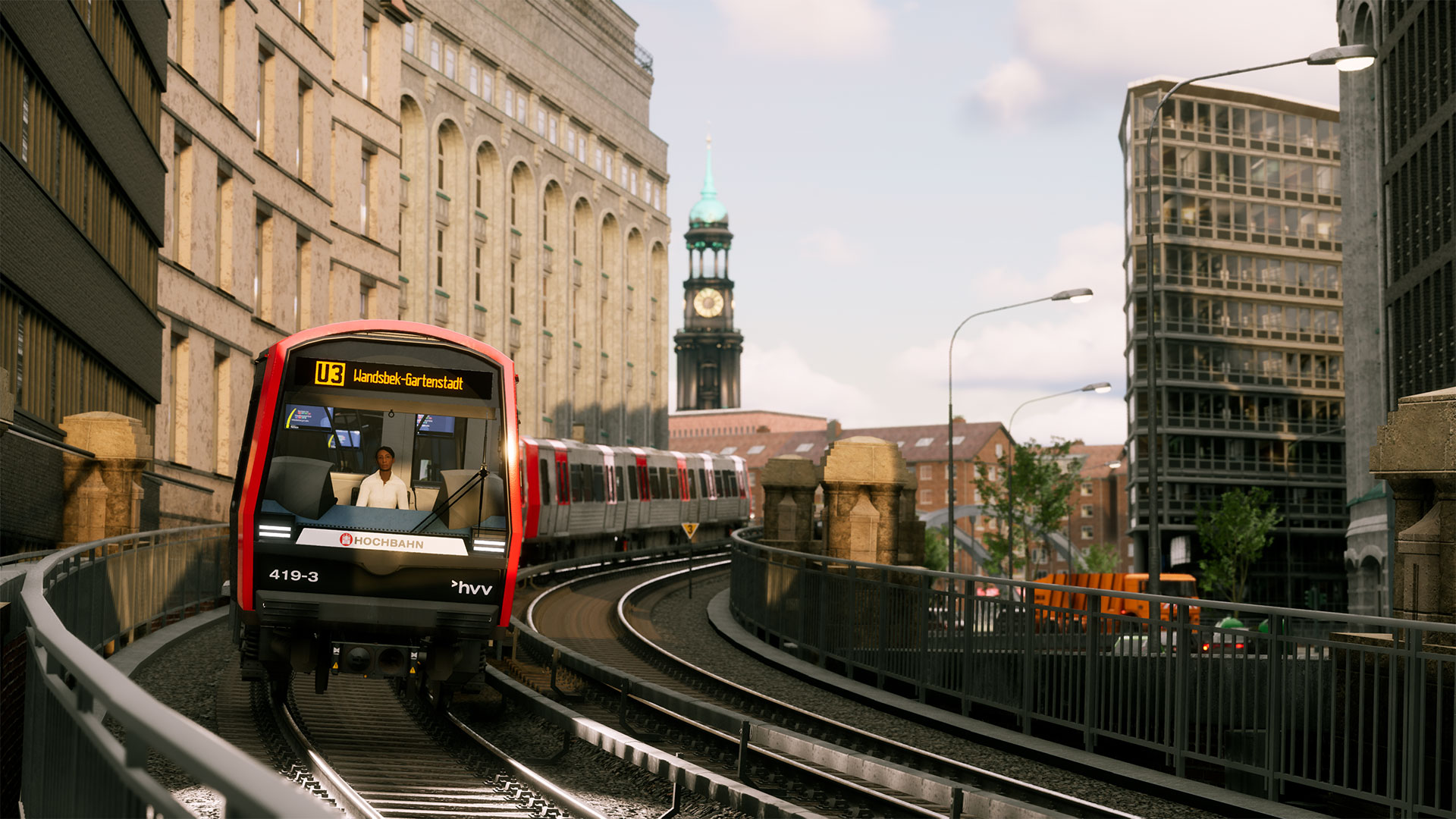 Ein rot-silberner Zug fährt auf Gleisen in einer Stadt. Gebäude säumen die Strecke, im Hintergrund ist ein Glockenturm zu sehen.