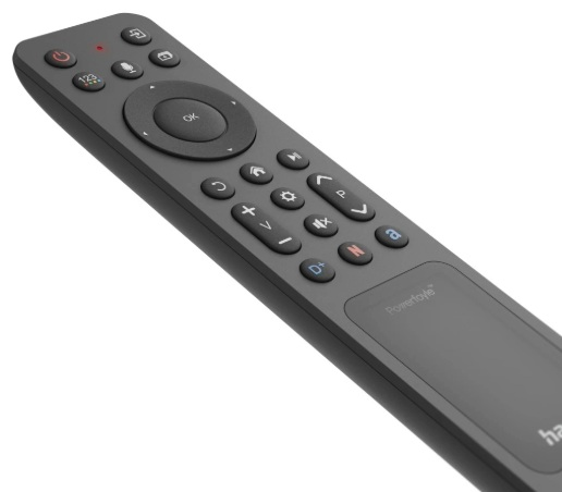 Ciemnoszary pilot z wieloma przyciskami, w tym zasilaniem, klawiszami kierunkowymi i regulacją głośności. Widoczny jest touchpad.