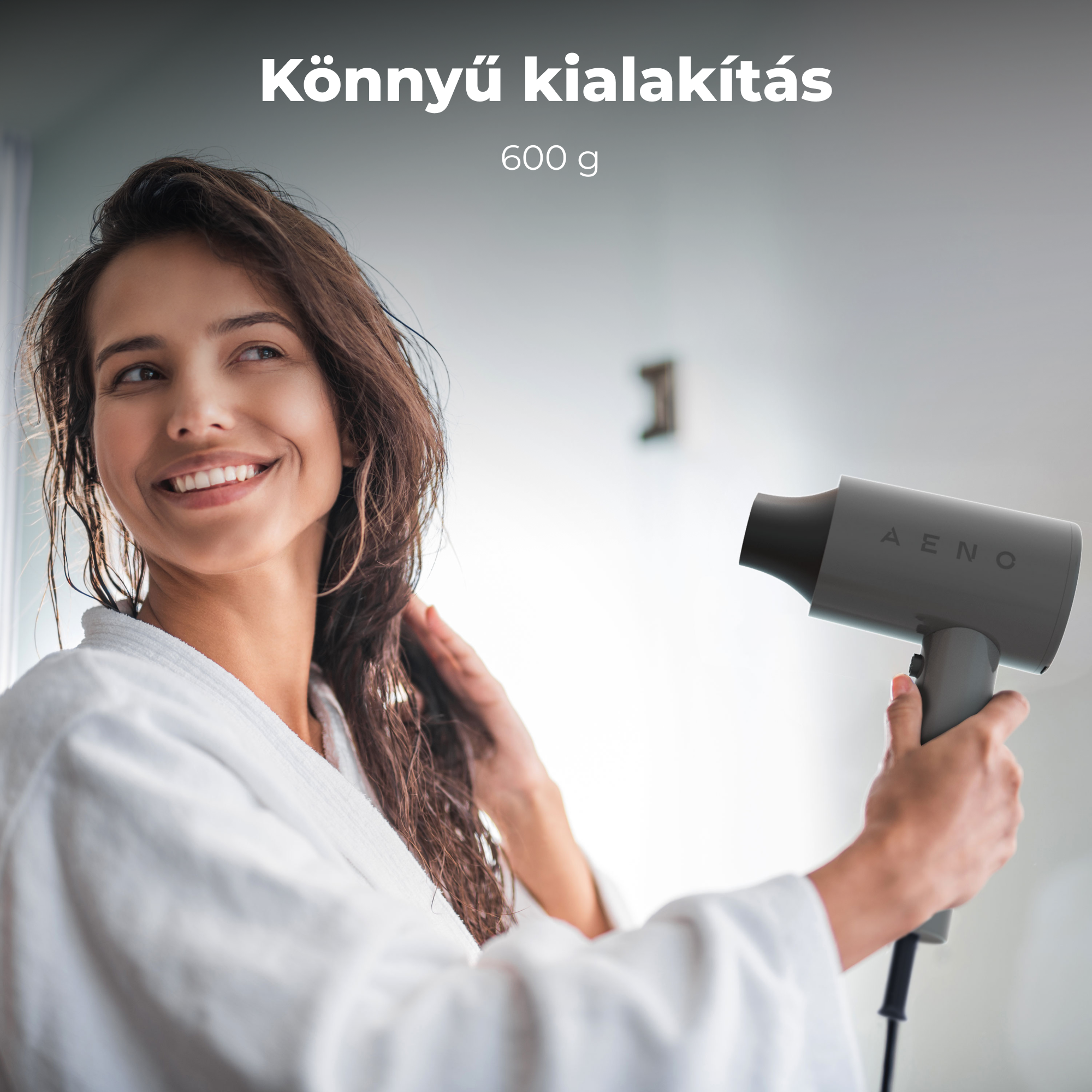 Fehér köntösös nő szürke hajszárítóval szárítja a haját. Mosolyog, elnéz. A háttér egy világos fal.