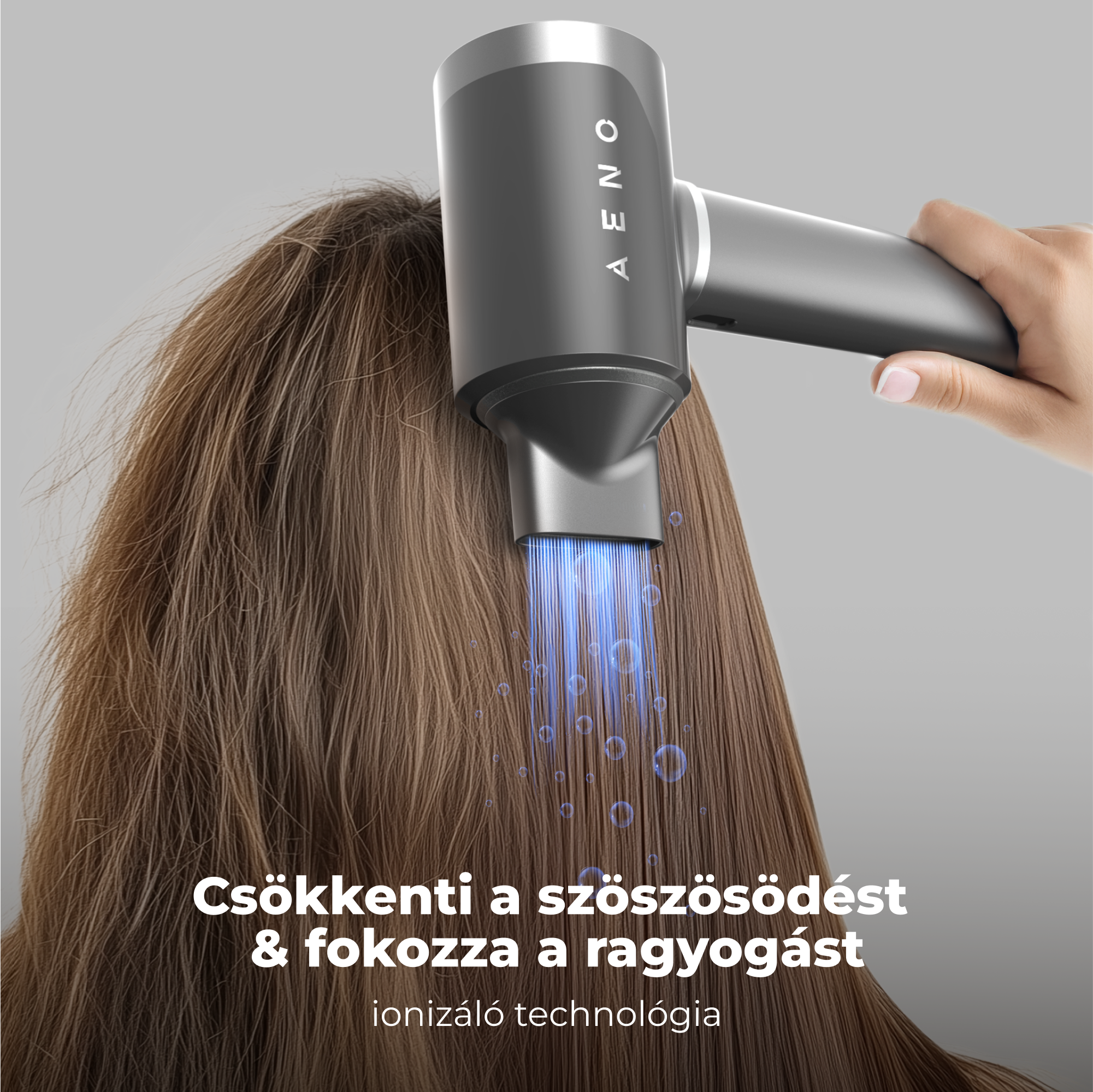 Egy hajszárító barna hajat szárít. A hajszárító szürke, AENO márkájú. Szöveg: Csökkenti a szöszt és fényt ad.