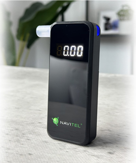 Czarny alkomat wyświetla '0,00'. Ma biały ustnik, widoczna marka 'NAVITEL'.