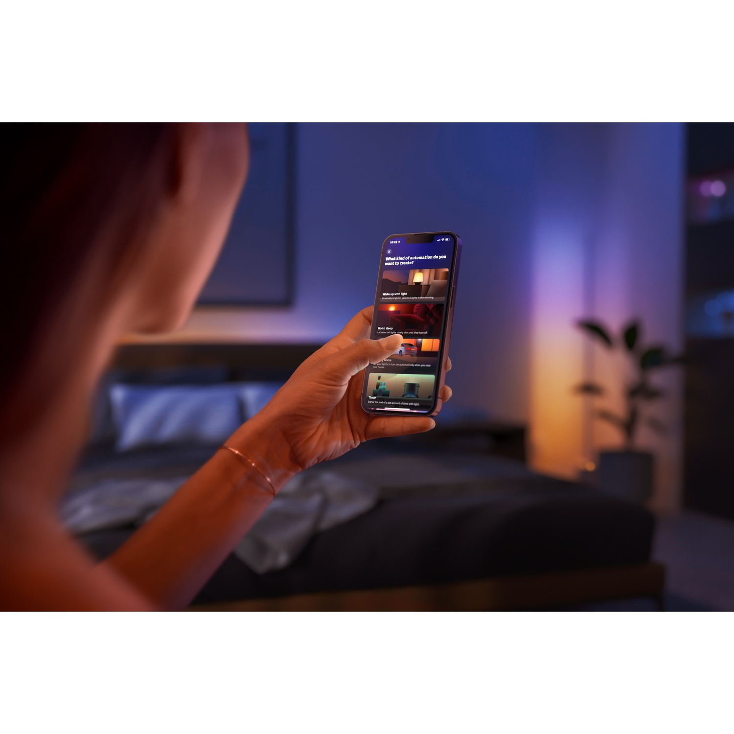 Una persona tiene in mano un telefono che mostra un'interfaccia dell'app. Lo schermo mostra opzioni come 'Svegliarsi con la luce' e 'Andare a dormire'.
