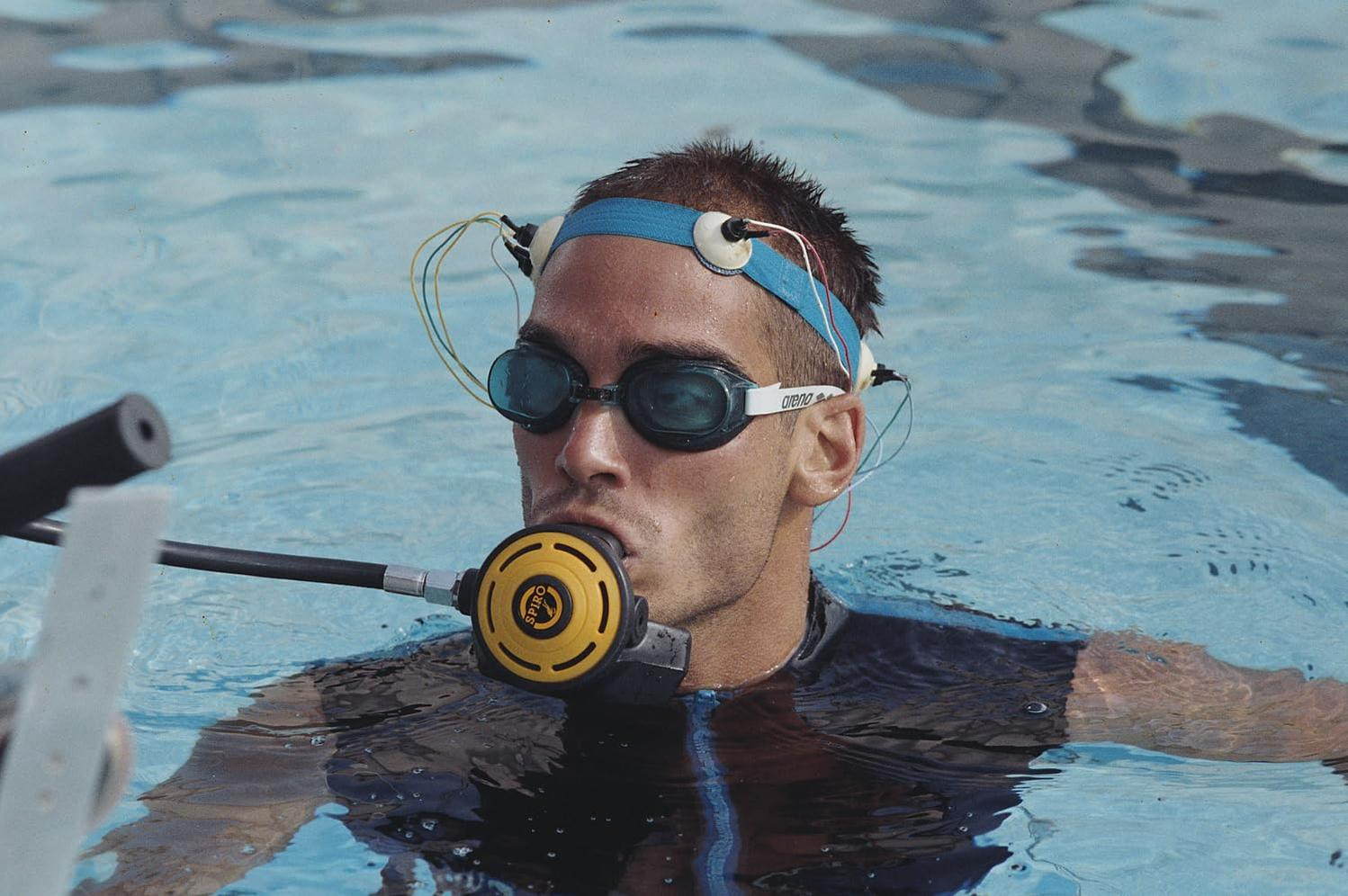 Ein Mann im Pool mit Brille, Stirnband mit Sensoren und Mundstück. Er ist im Wasser, mit einem schwarzen Schlauch.