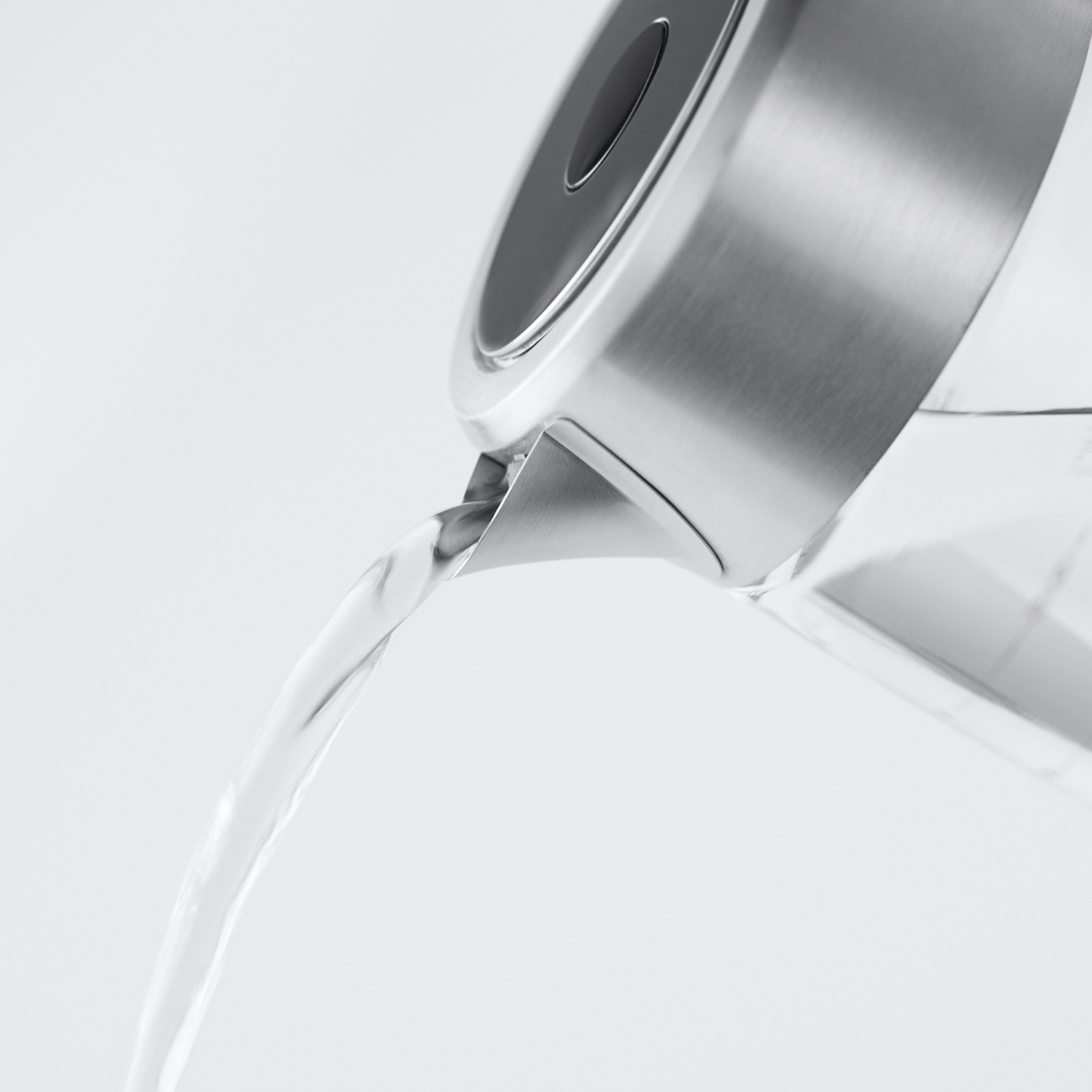 Un bollitore in acciaio inossidabile versa acqua. Il bollitore è argentato con un coperchio nero. L'acqua esce su uno sfondo bianco.