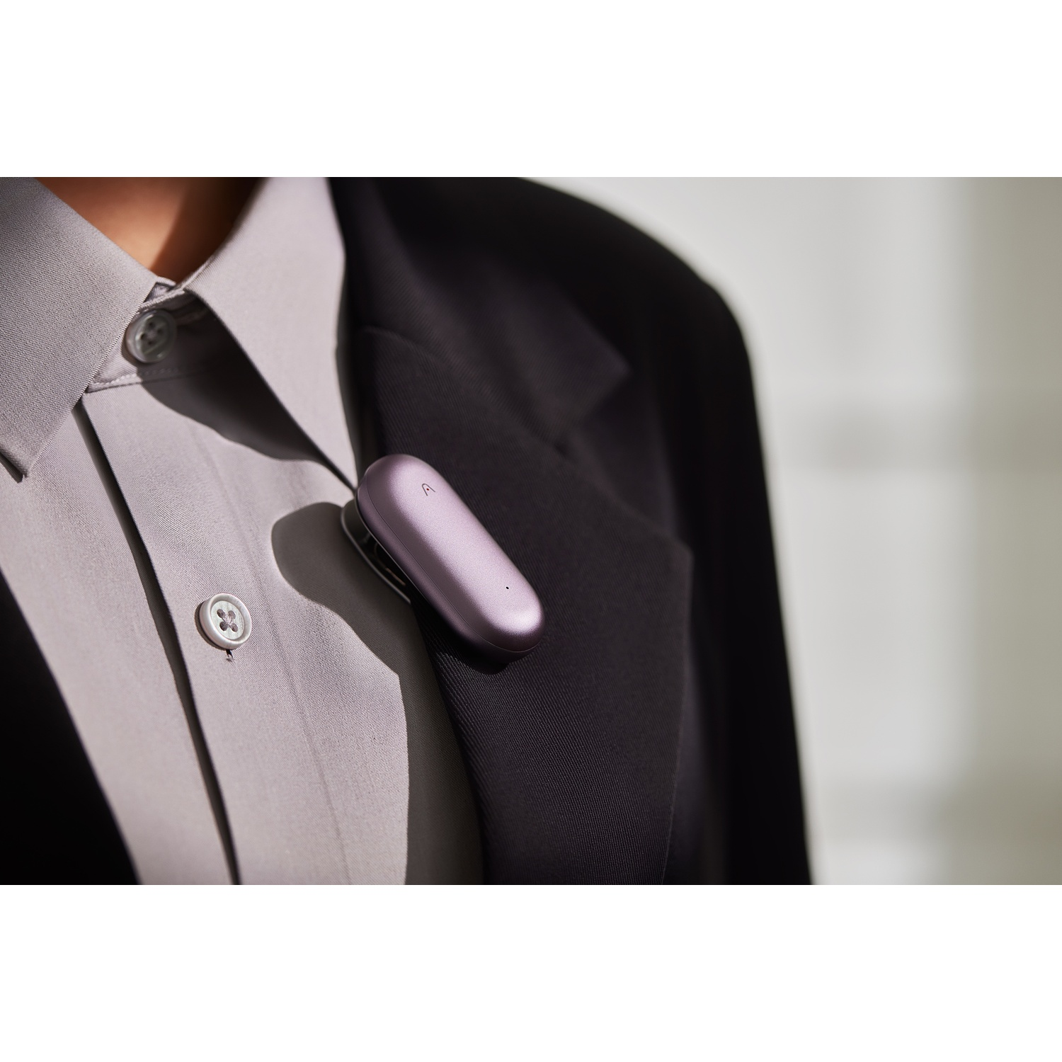 Un dispositivo color lavanda attaccato a una camicia grigia e un blazer nero. La camicia ha un colletto abbottonato.
