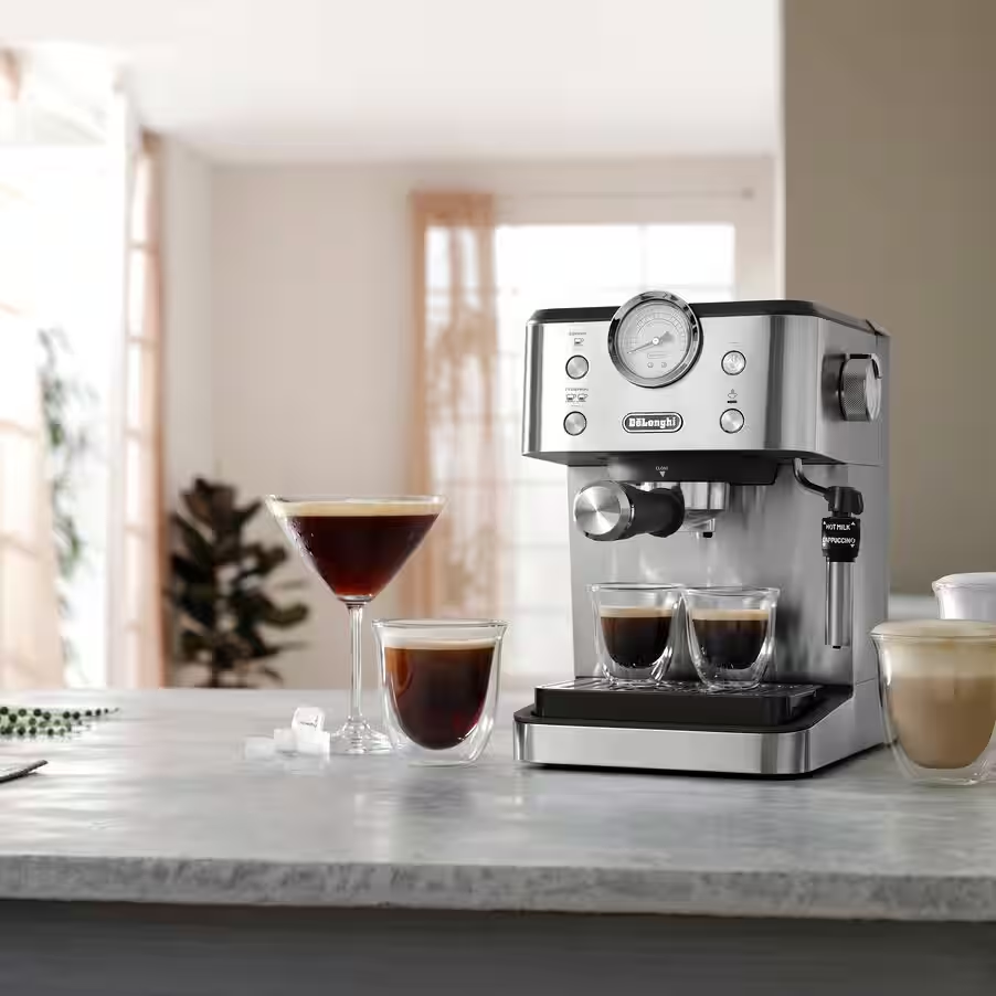 Egy ezüst eszpresszó gép kávéval a poharakban. Egy martini pohár kávéval és egy latte csésze is az asztalon van.