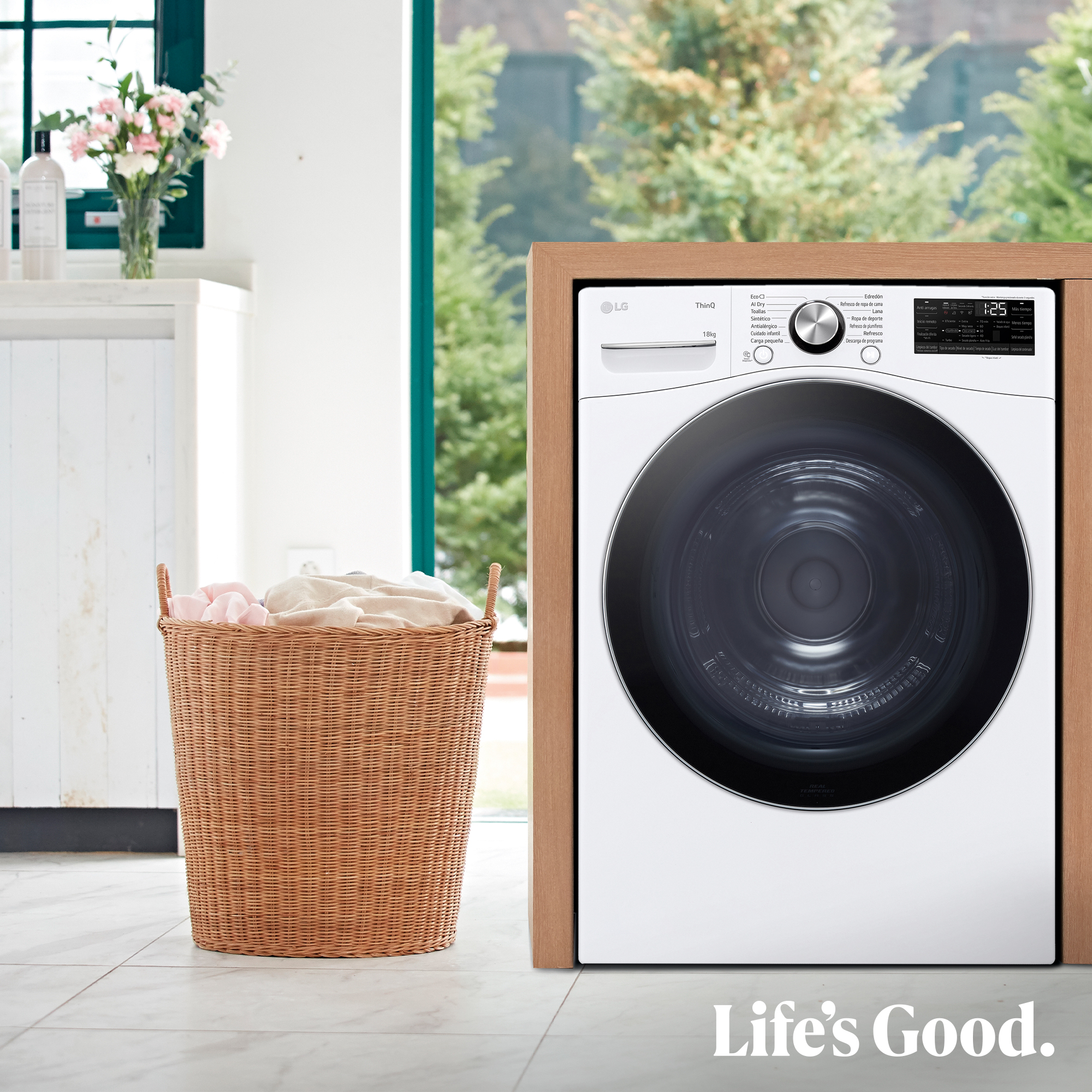 Una lavadora junto a una cesta de ropa. Flores en el fondo. Las palabras 'Life's Good' están en la parte inferior.