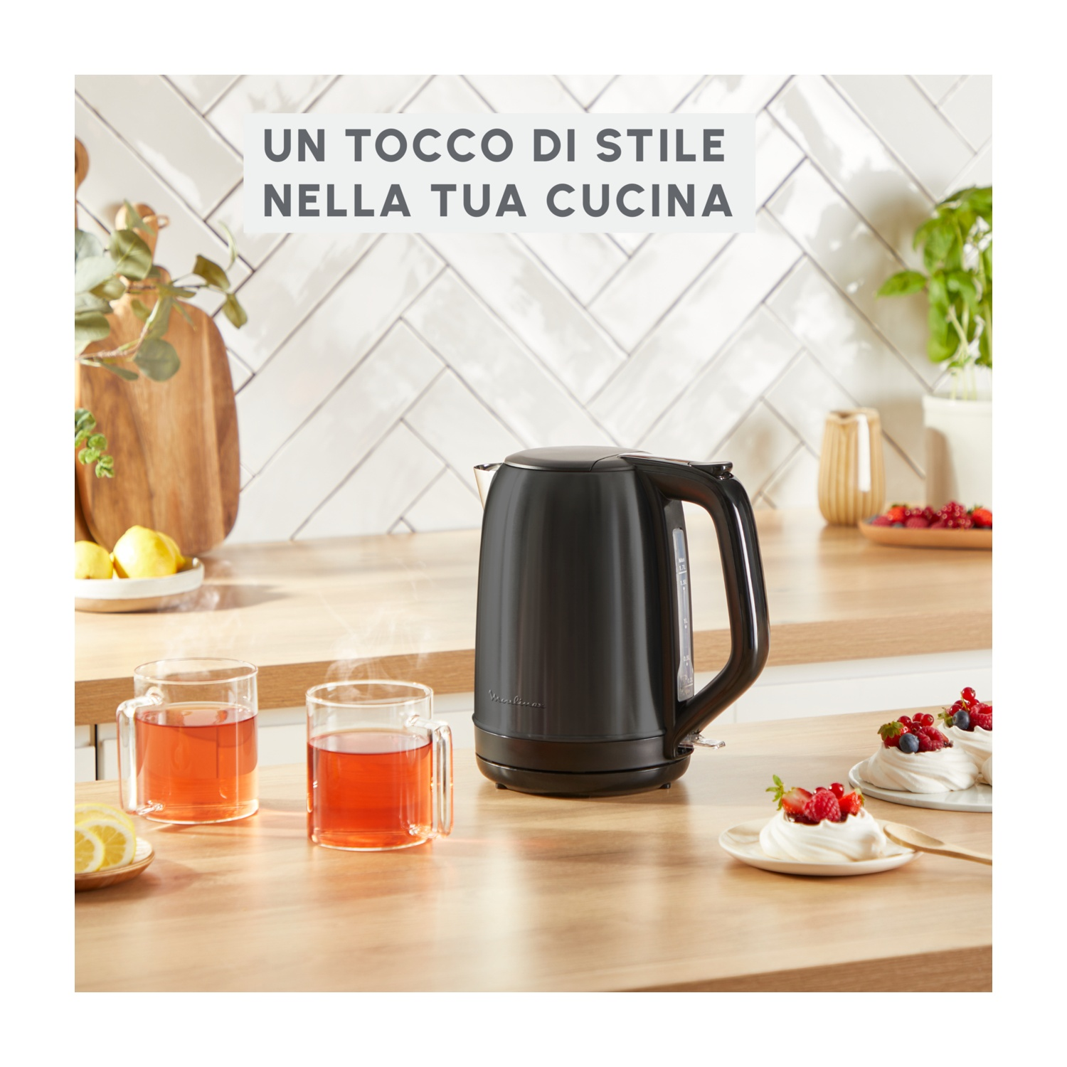 Un bollitore nero, due bicchieri con liquido rosso e dessert su un tavolo di legno in un ambiente cucina.