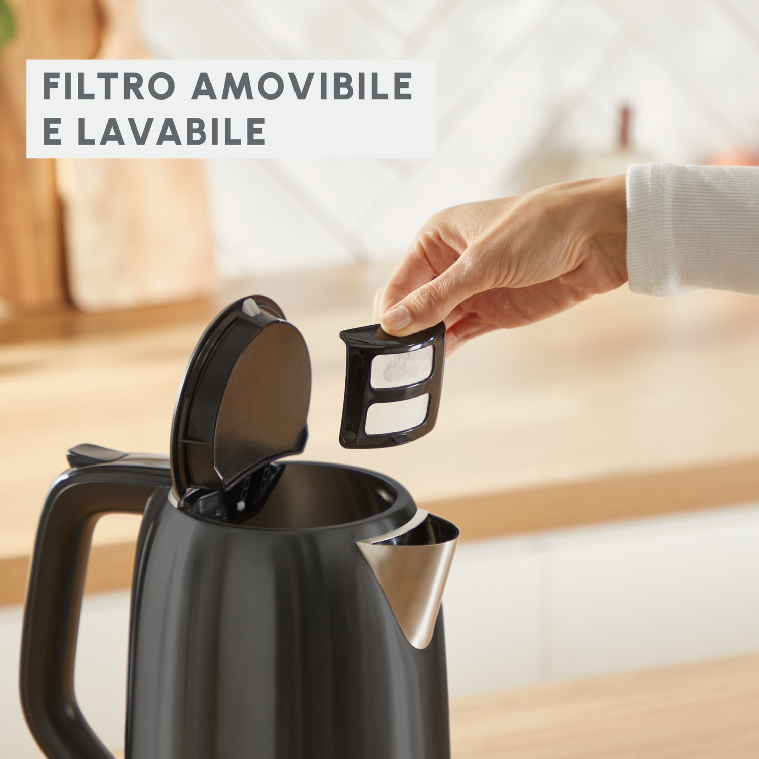 Una mano rimuove un filtro da un bollitore nero. Il bollitore è aperto e il filtro è nero con maglia bianca. Testo: "rimovibile e lavabile".