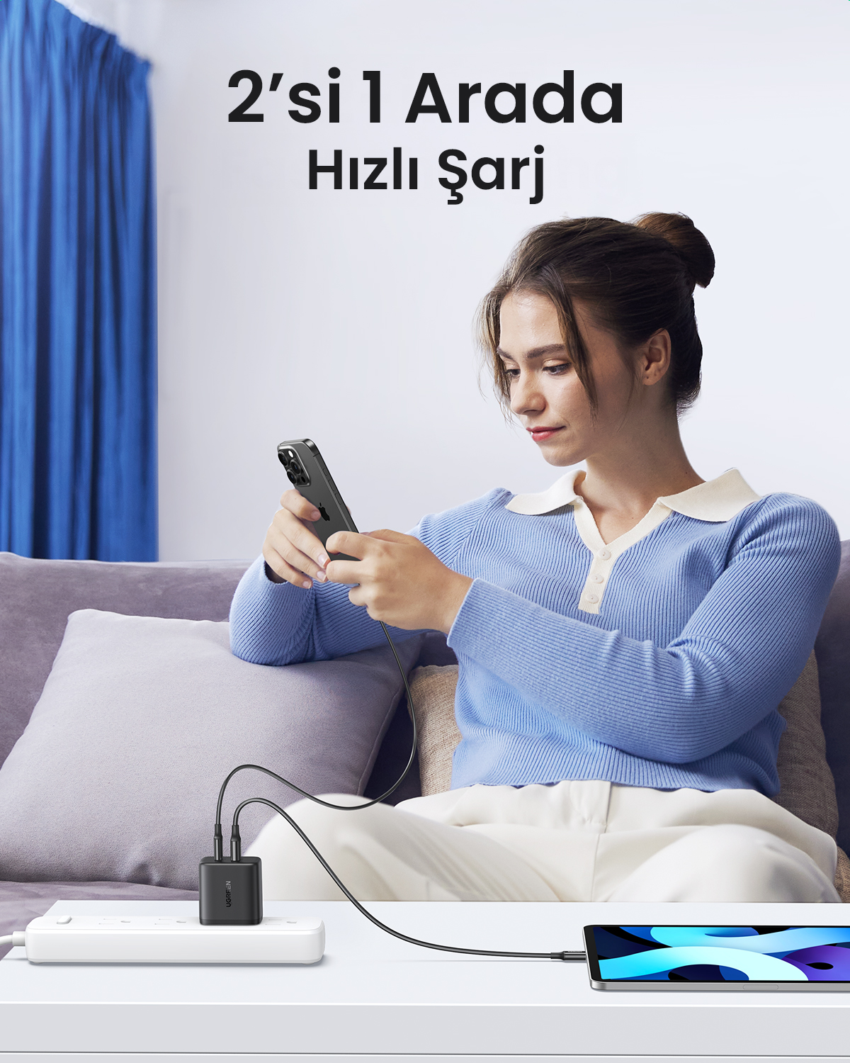 Bir kadın, bir şarj cihazına bağlı bir telefon kullanırken kanepede oturuyor. Bir tablet de şarj oluyor. Metinde '2'si 1 Arada Hızlı Şarj' yazıyor.
