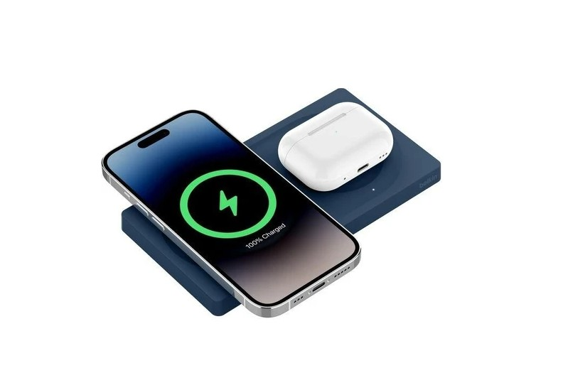 Kablosuz şarj olan bir telefon, %100 şarj gösteriyor. Beyaz bir kulaklık kılıfı, telefonun yanında şarj cihazının üzerinde duruyor.
