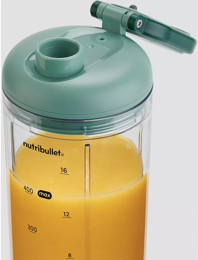 Egy zöld Nutribullet turmixgép narancslével töltve. A turmixgép átlátszó műanyag tartálya méretekkel ellátott.