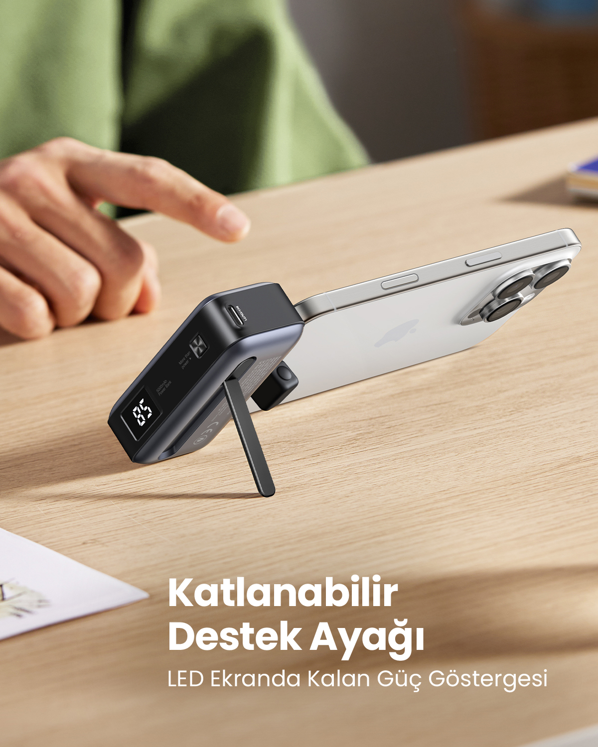 Telefon, katlanabilir bir stand ile siyah bir powerbank'e yaslanmış. Bir el, powerbank'i gösteriyor. Telefonun altında metin var.