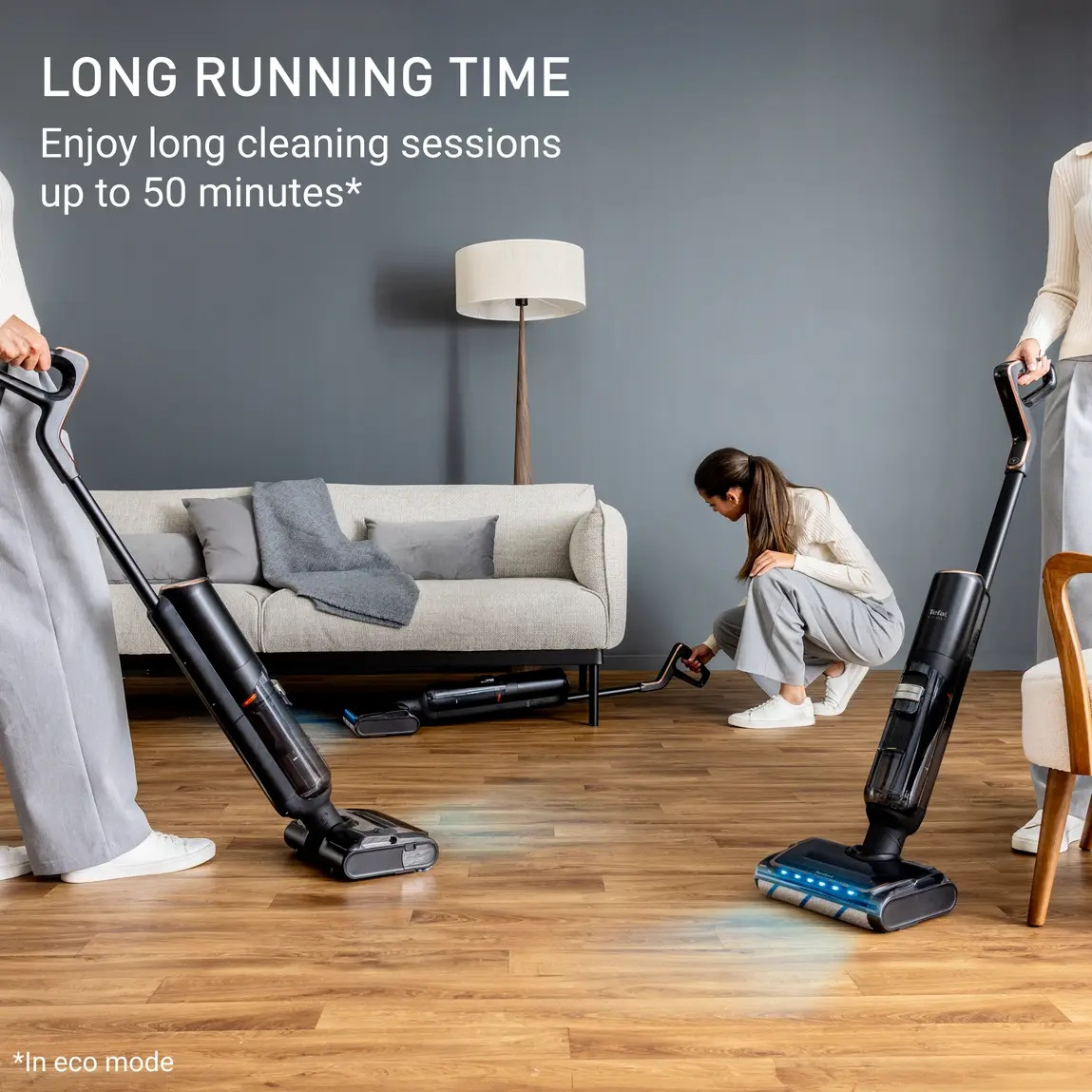 Trzy osoby używają odkurzaczy na drewnianej podłodze. W tle sofa, lampa i tekst o długich sesjach sprzątania.