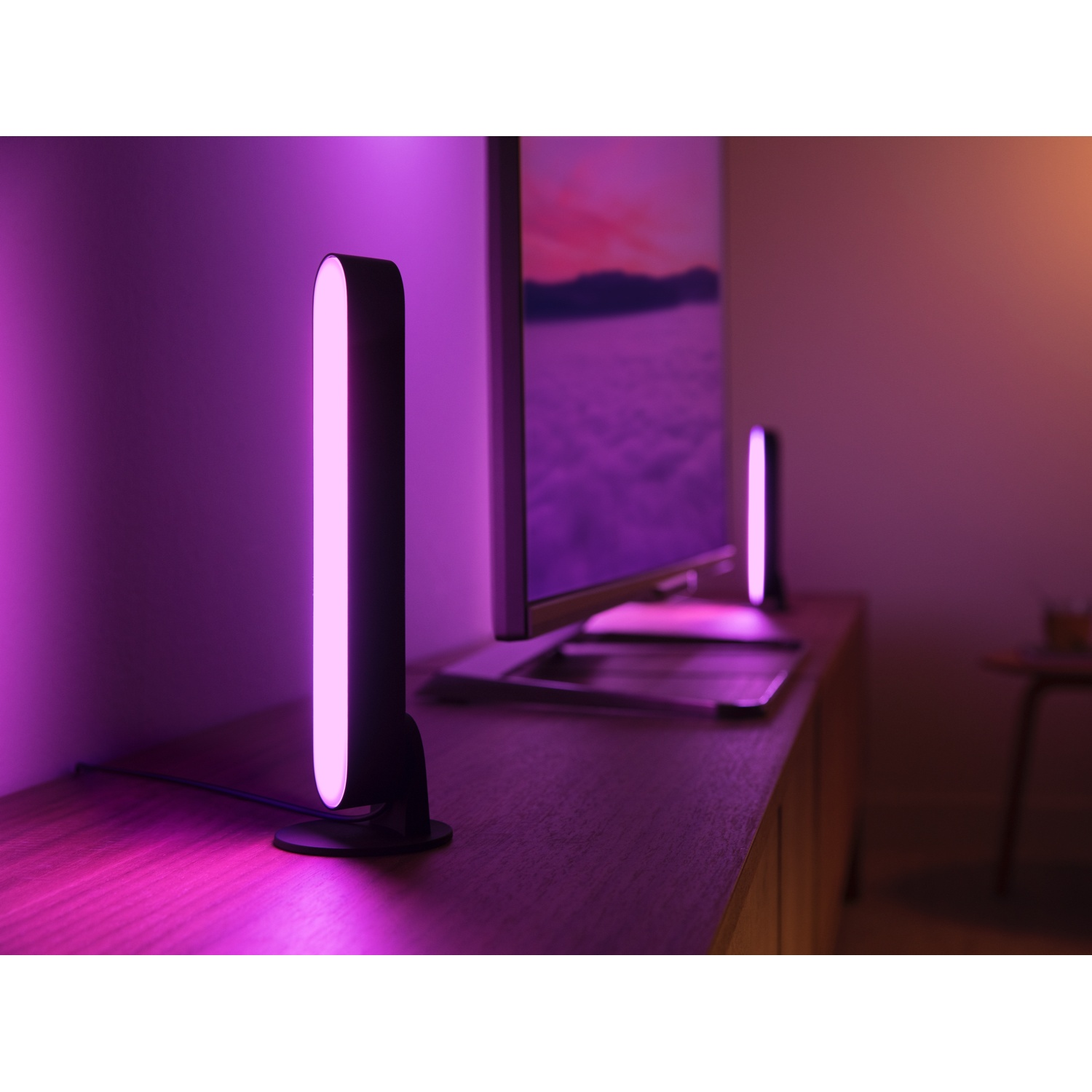 Una TV è su un mobile di legno, con due barre luminose nere illuminate. La scena è immersa in luce rosa e viola.