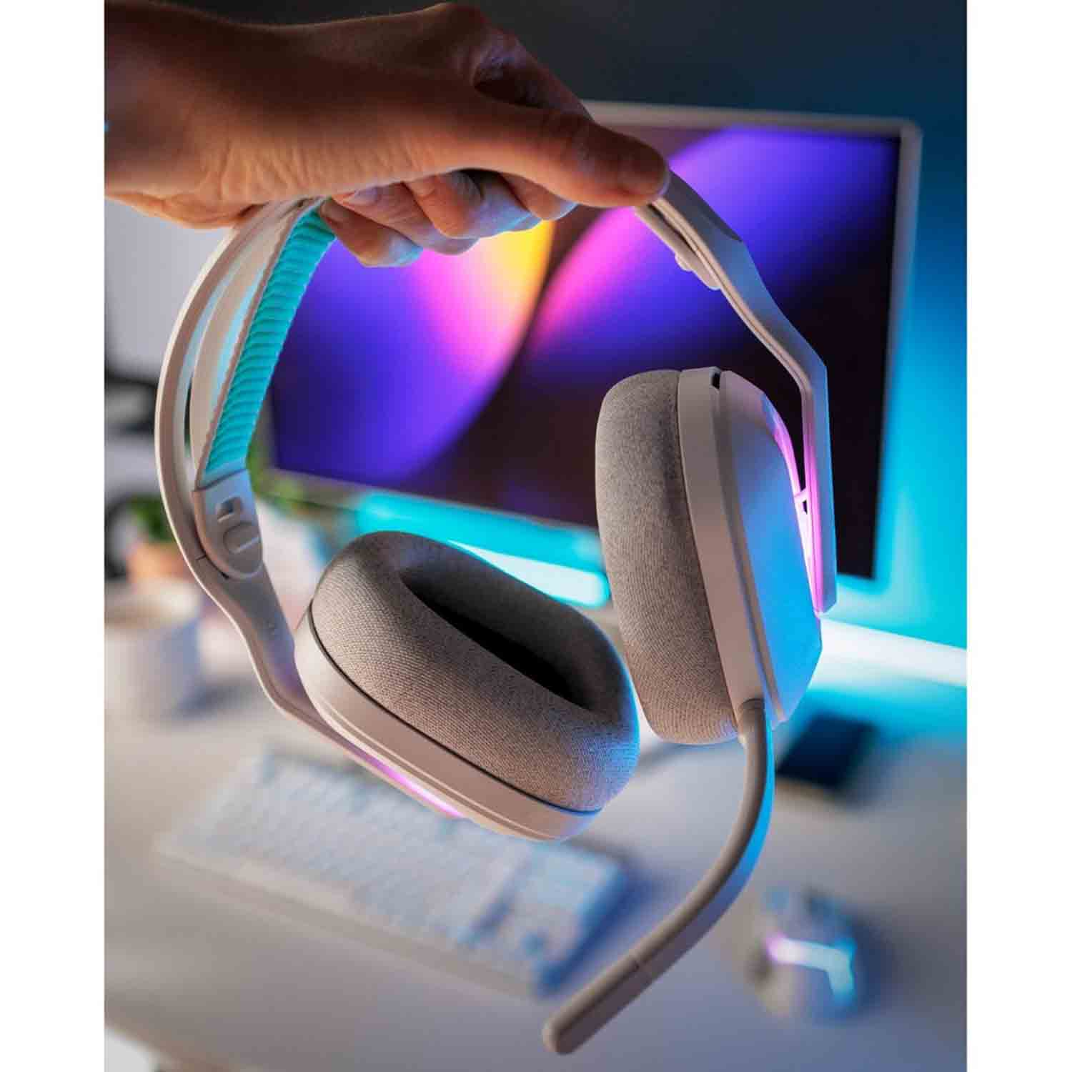 Mano che tiene cuffie bianche e grigie, con un accento azzurro. Lo sfondo mostra un monitor di computer e una tastiera.