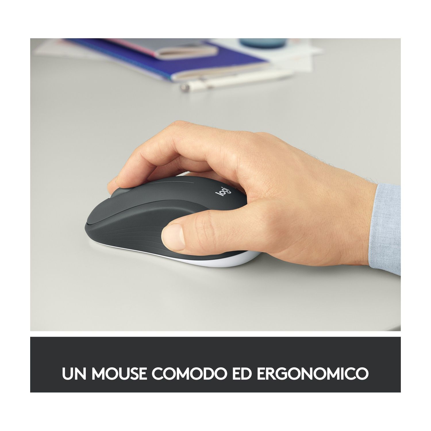 Mano che tiene un mouse Logitech grigio su una superficie bianca. Il mouse ha una base bianca. Lo sfondo presenta carte e una penna.