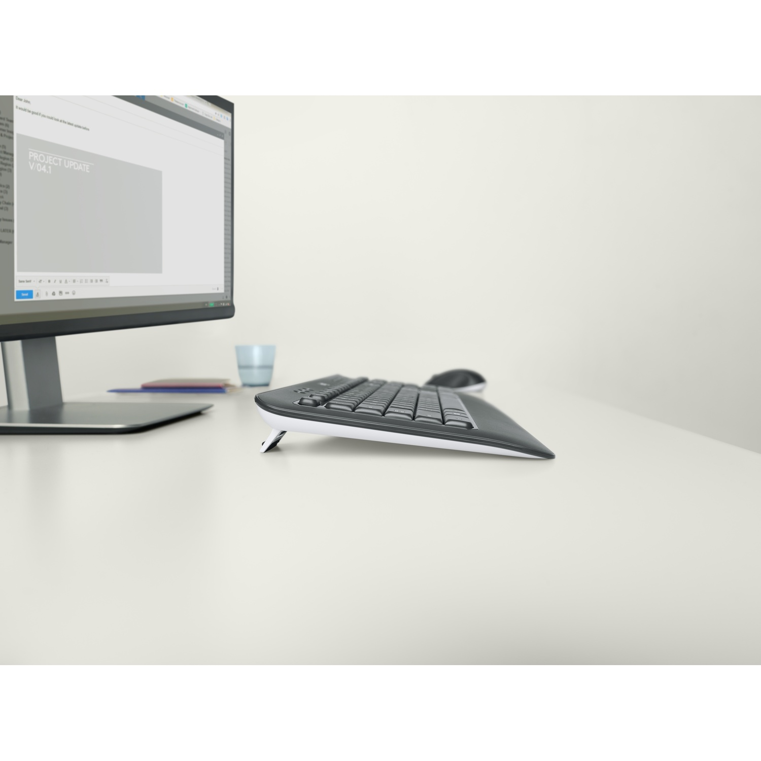 Un'area di lavoro con tastiera, mouse e monitor che mostra un aggiornamento del progetto. Sul tavolo sono visibili anche un bicchiere d'acqua e una penna.