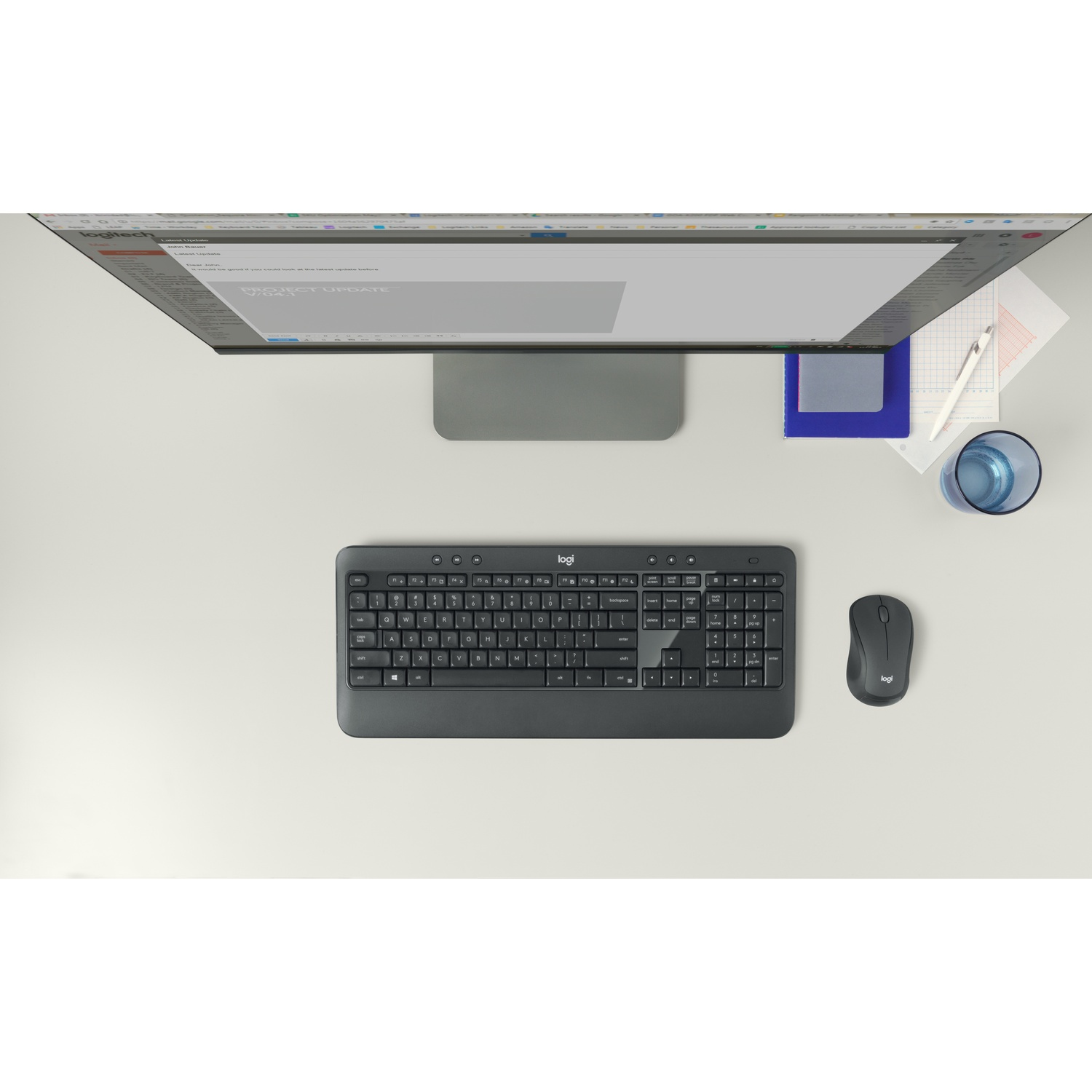 Vista dall'alto di una scrivania con un monitor che mostra un'e-mail. Sono presenti una tastiera, un mouse, un bicchiere d'acqua e dei fogli.