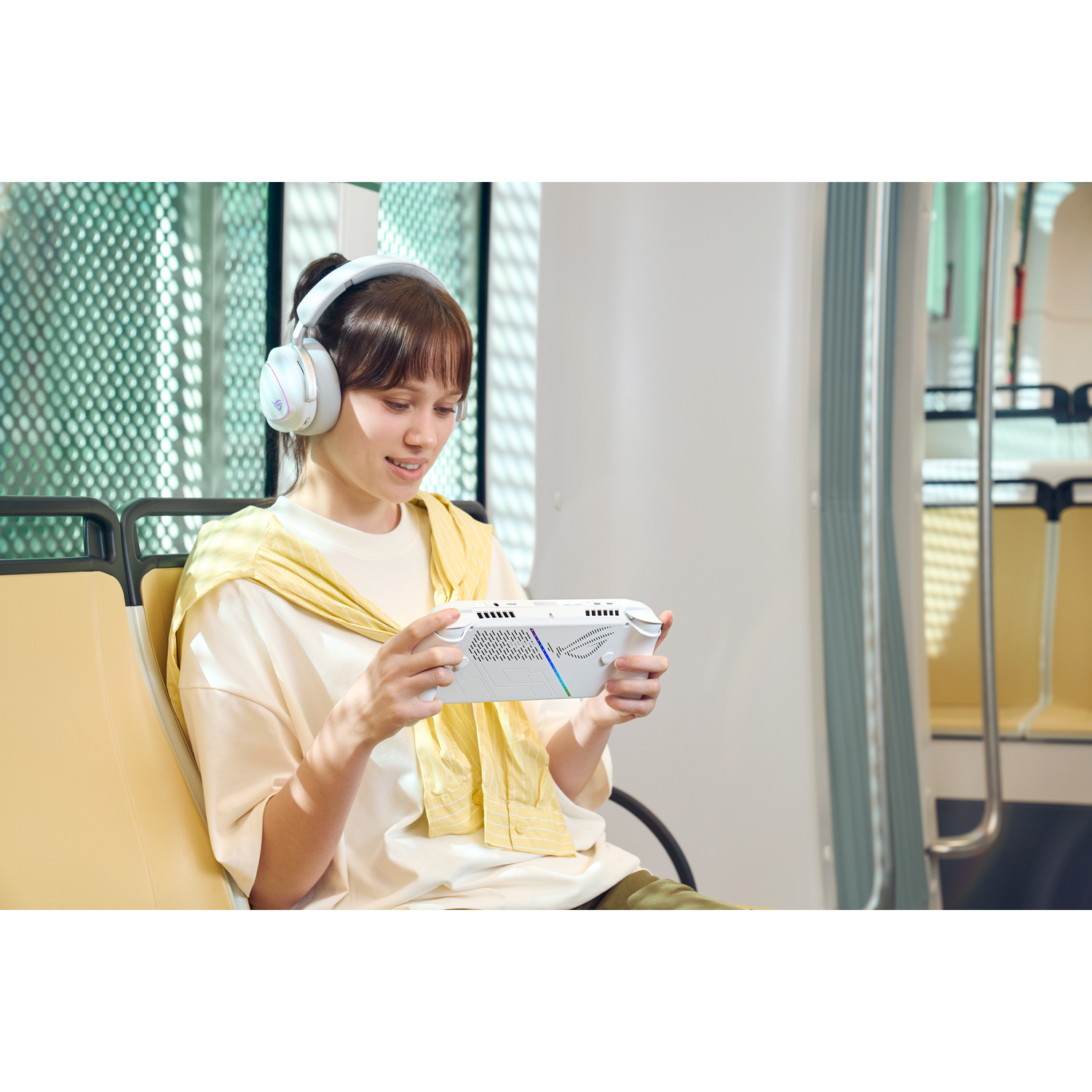Een vrouw met een koptelefoon speelt op een handheld console in een trein. Ze glimlacht en houdt de console met beide handen vast.