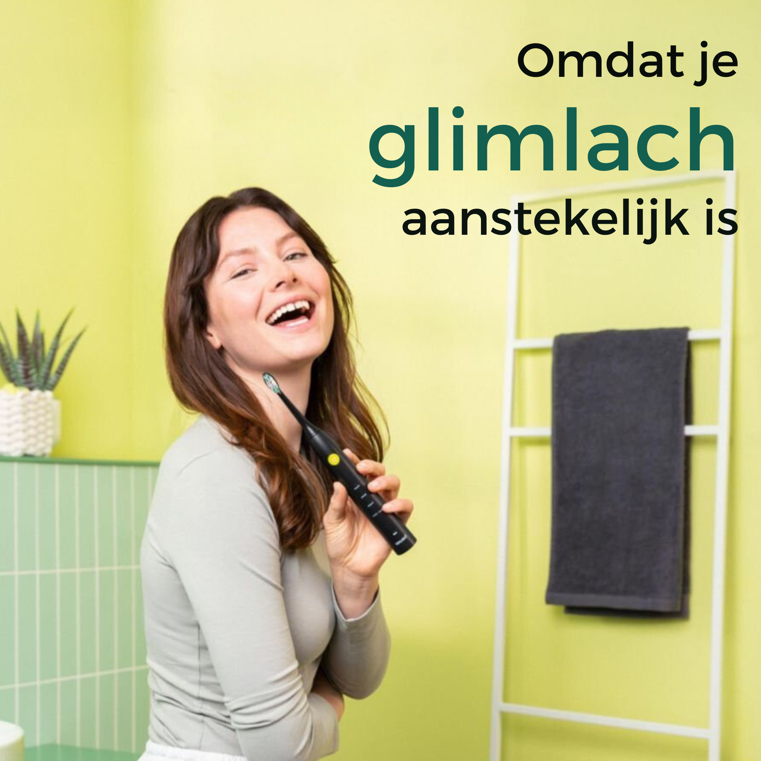 Woman smiling, holding a black toothbrush. Text says 'Because your smile is contagious'. Background: green, towel rack, and plant.