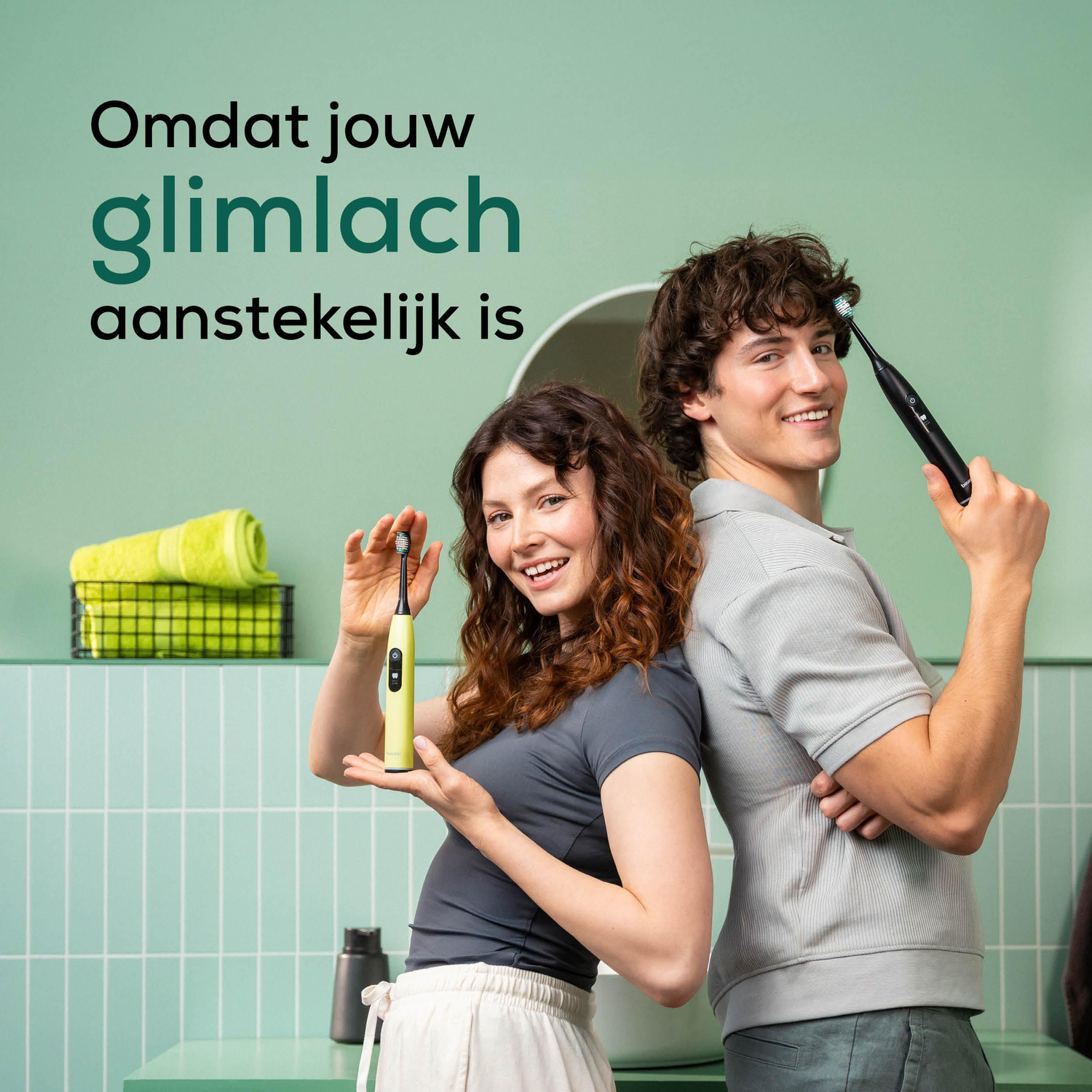 A couple smiles holding toothbrushes. Woman holds green one, man holds black. Green wall with text above.