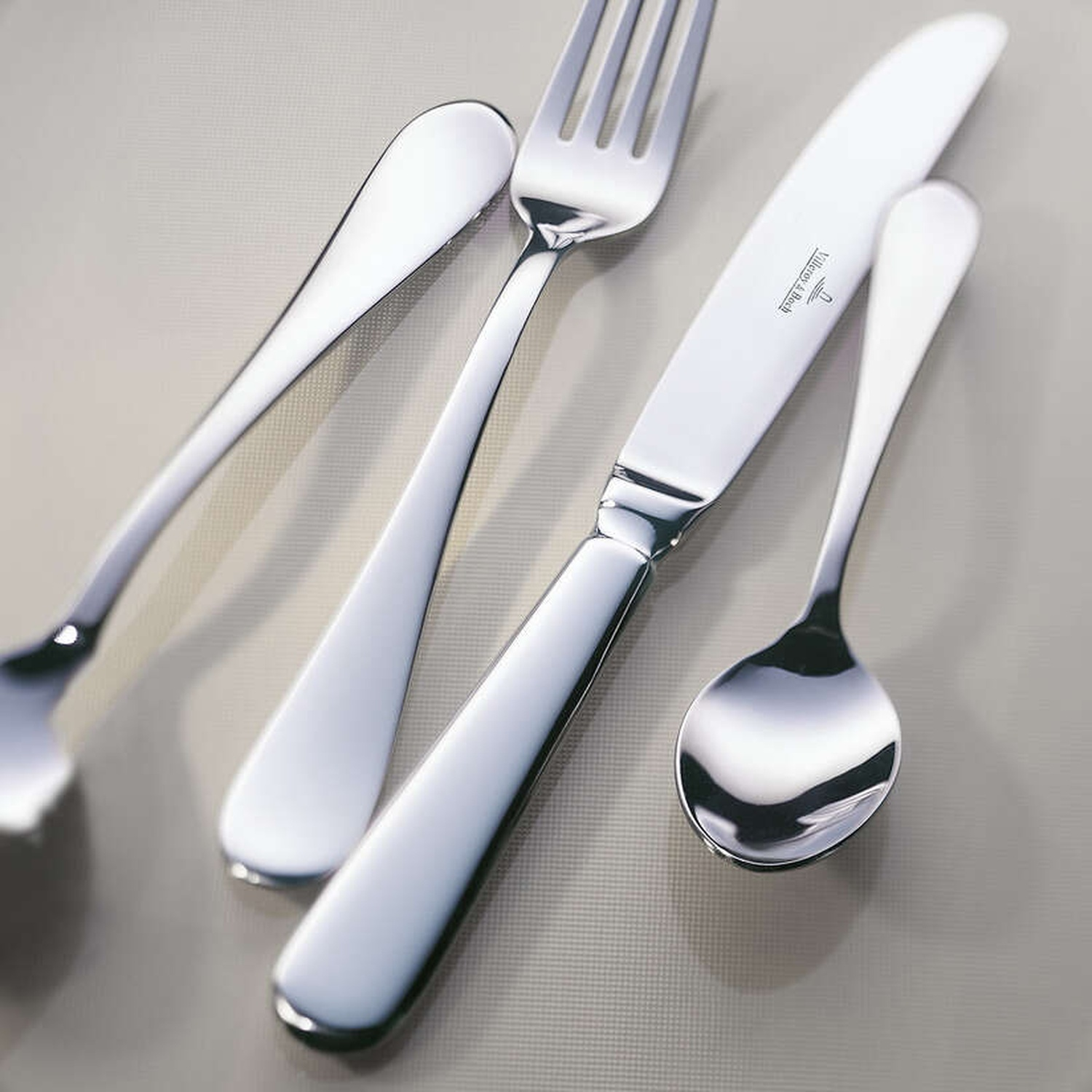 Gros plan sur des couverts sur une surface gris clair. Comprend une fourchette, un couteau et une cuillère. Les couverts sont brillants et réfléchissants.
