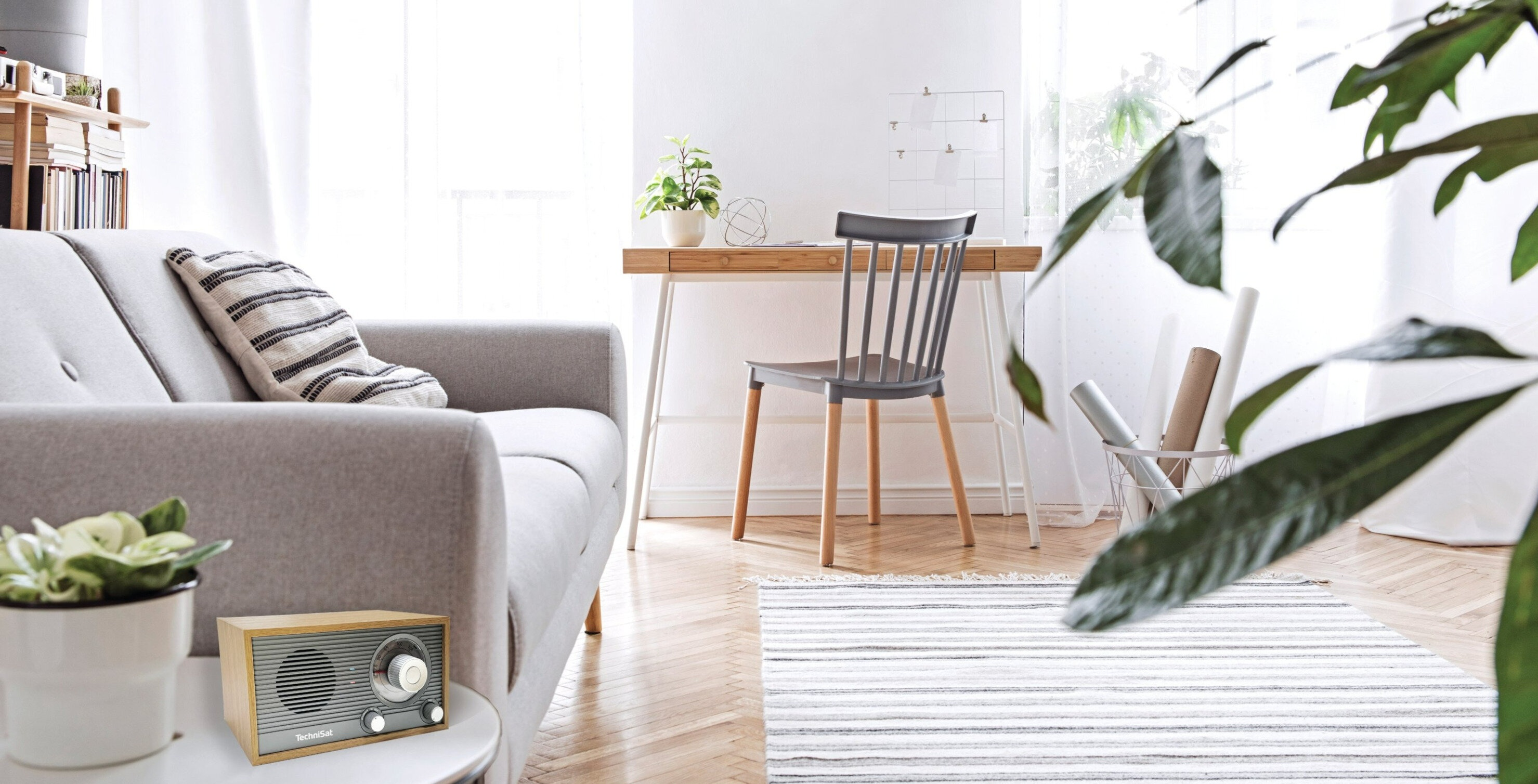 Nowoczesny salon z szarą sofą, drewnianym biurkiem, krzesłem, dywanem i radiem na stoliku.