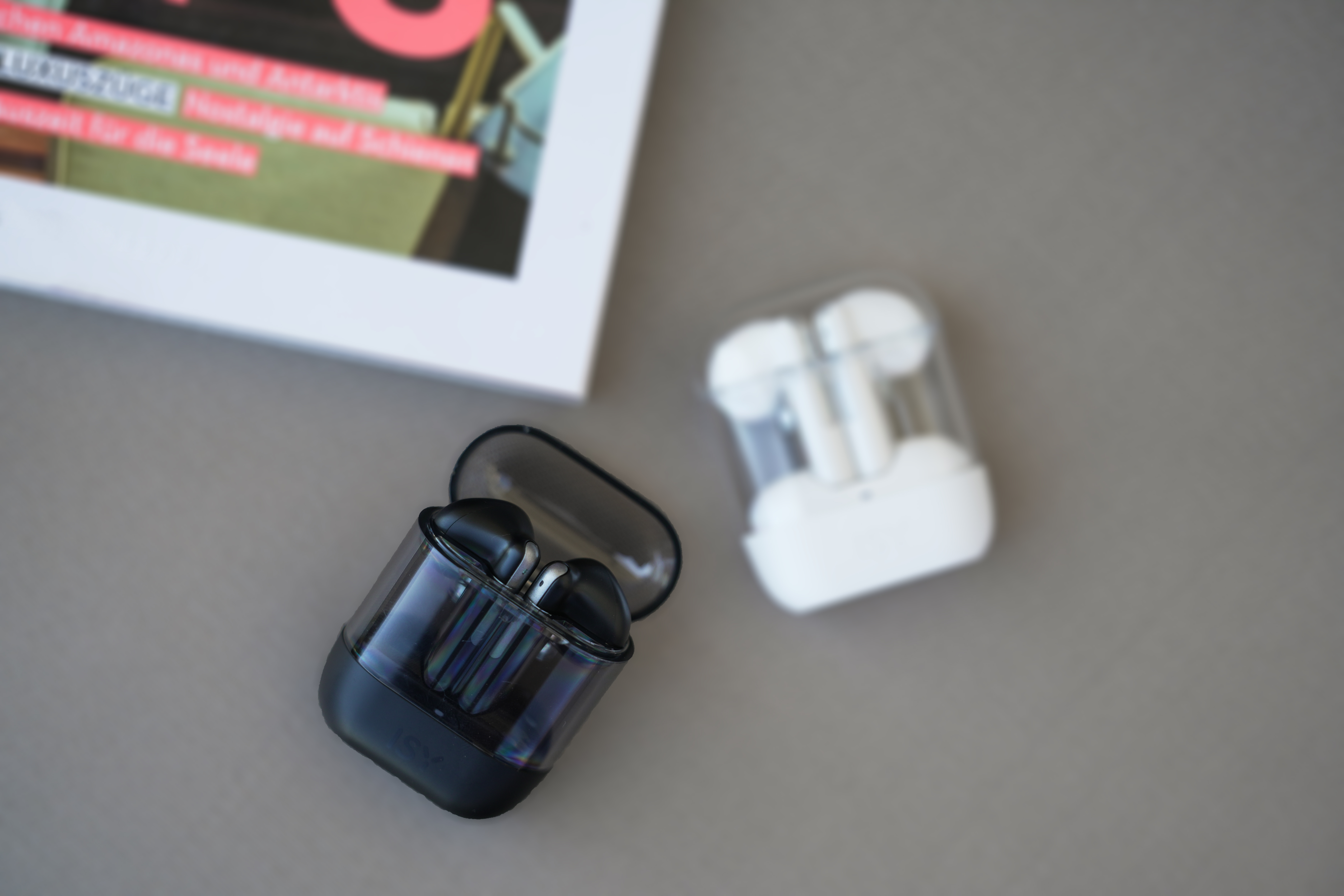 Dwa zestawy słuchawek w przezroczystych etui. Jeden czarny, jeden biały. Książka w tle.