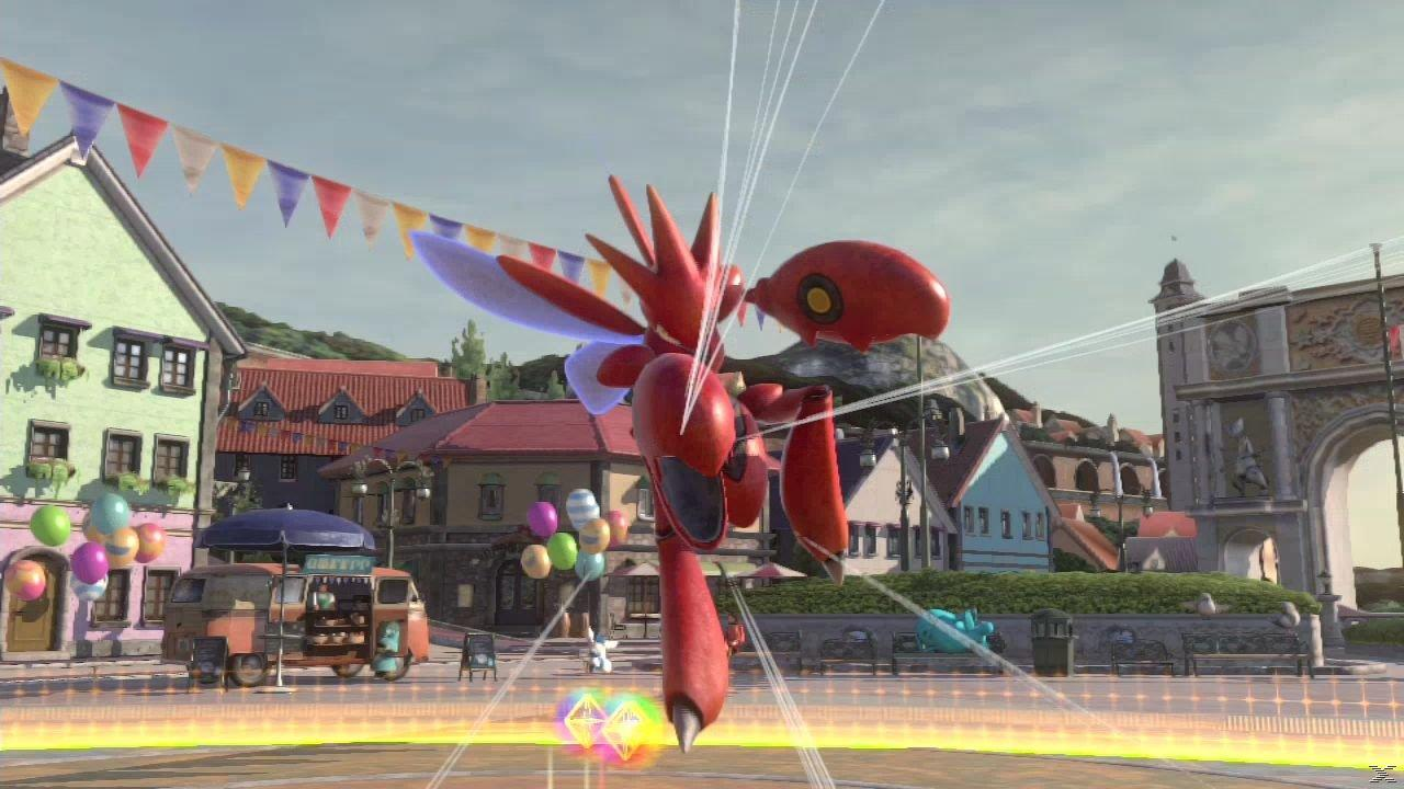 Czerwony robot ze skrzydłami stoi na placu. Otaczają go budynki. Widoczna jest furgonetka z jedzeniem i balony. Niebo jest czyste.